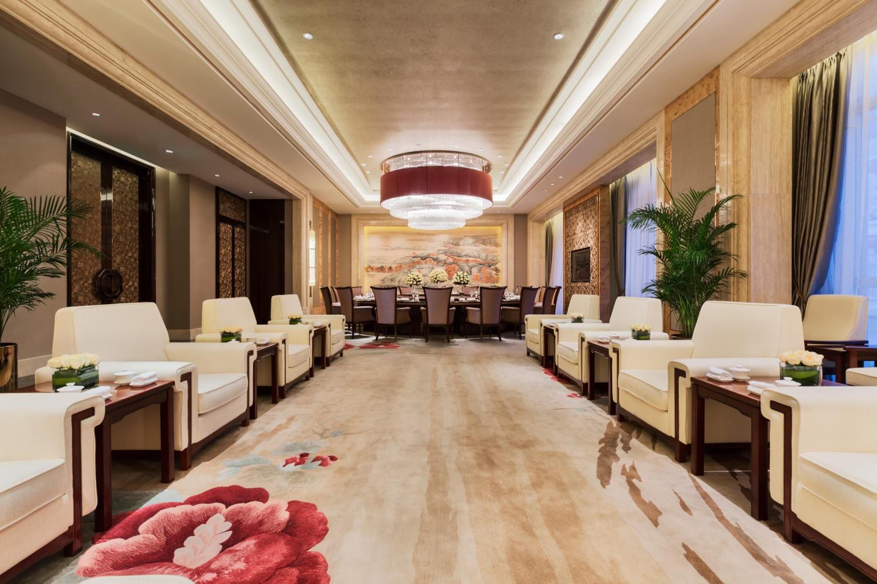 Een hotel lobby met een centrale eetruimte, zithoekjes en een kroonluchter.