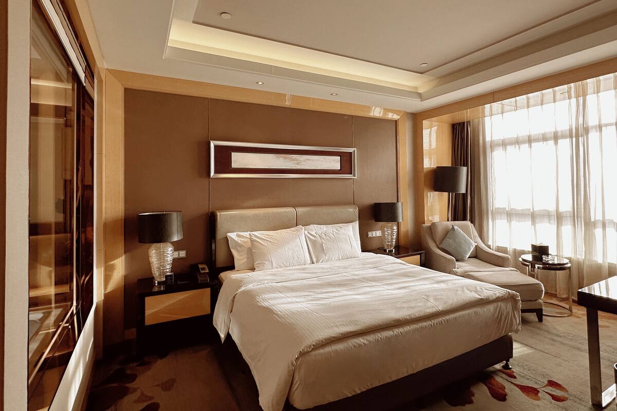 A hotel room with a large bed, two bedside tables, a chair, a desk, and a large window with curtains.