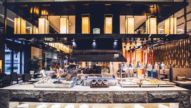 A buffet setup with various food items and utensils, a central cooking area, and a seating area with tables and chairs. - Wanda Realm Dandong (Dandong)