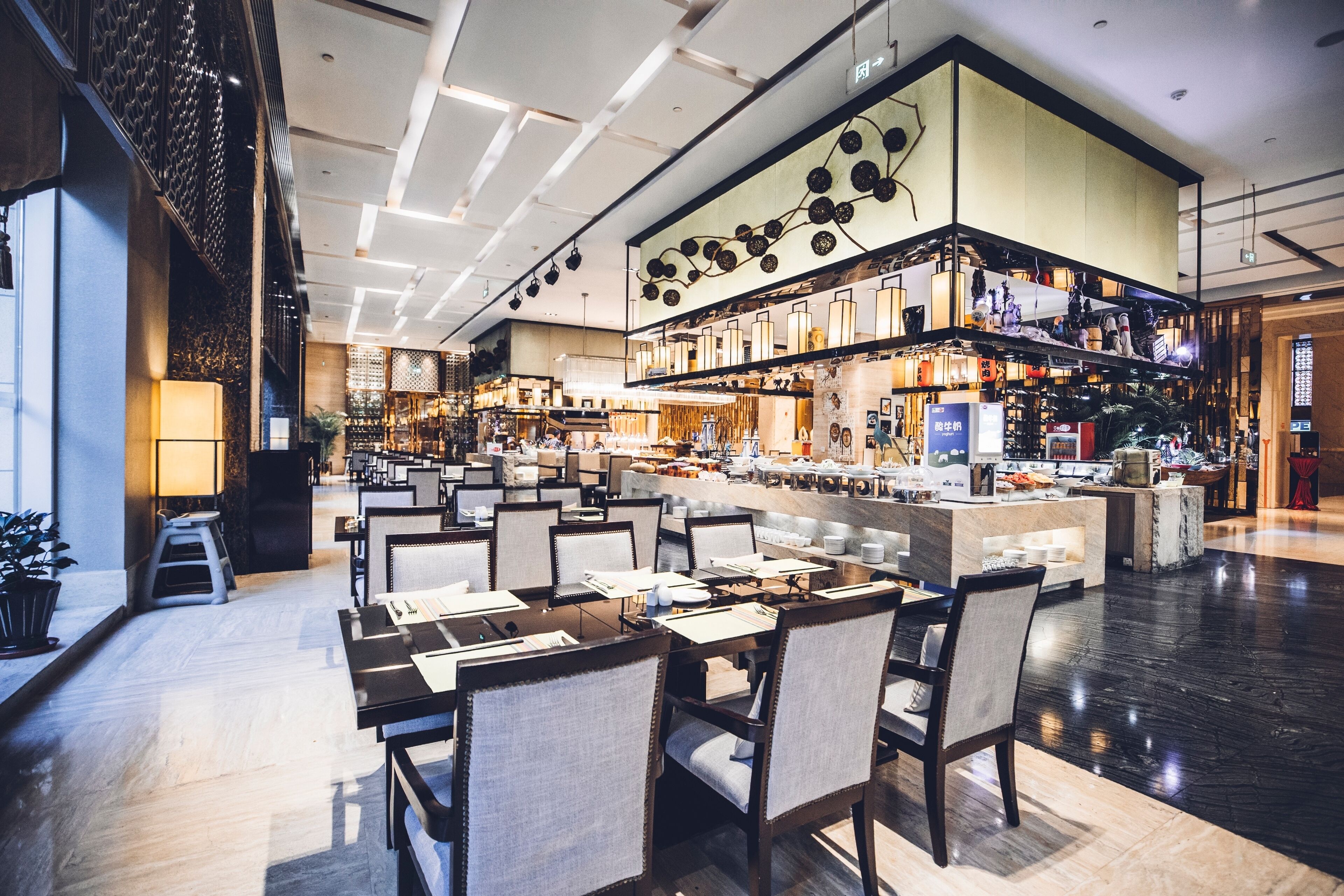 Un hall de hotel amplio con varias zonas de estar, un bar central y una escalera que conduce a un nivel superior.