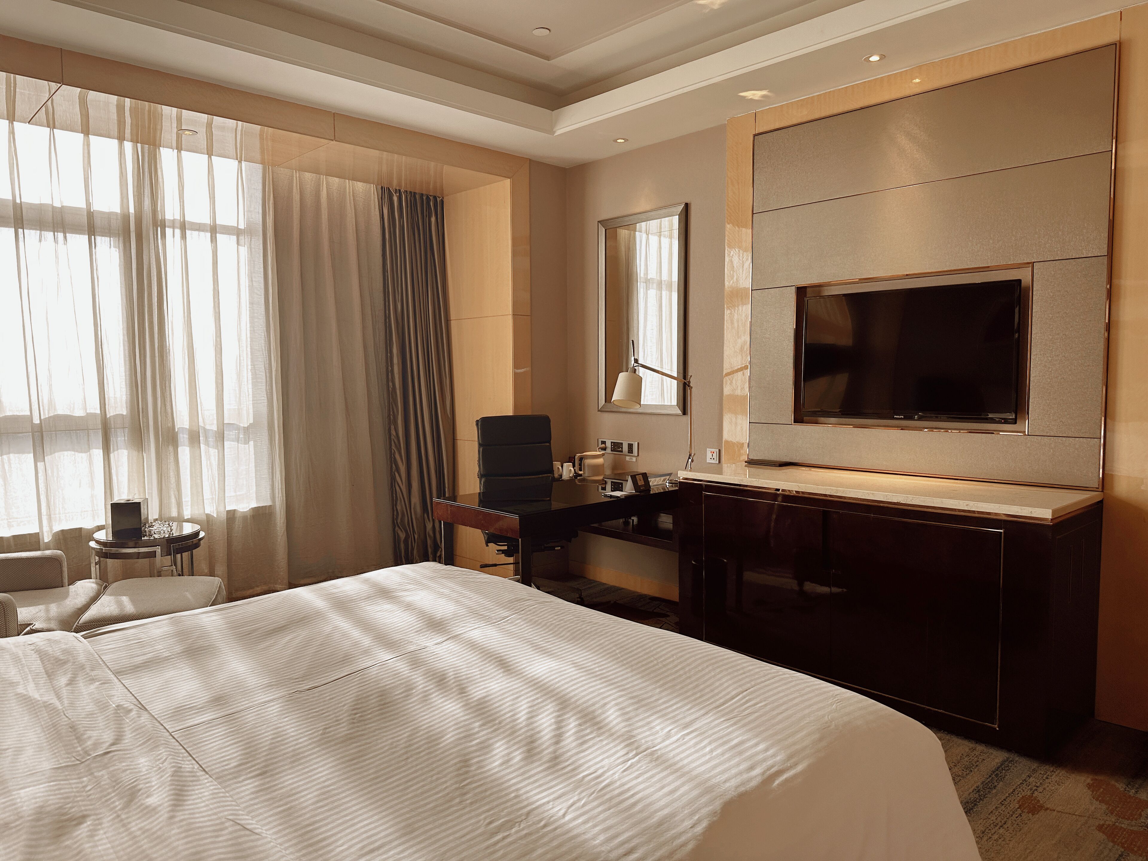 A hotel room with a large bed, a desk with a chair, a television, and a window with curtains.