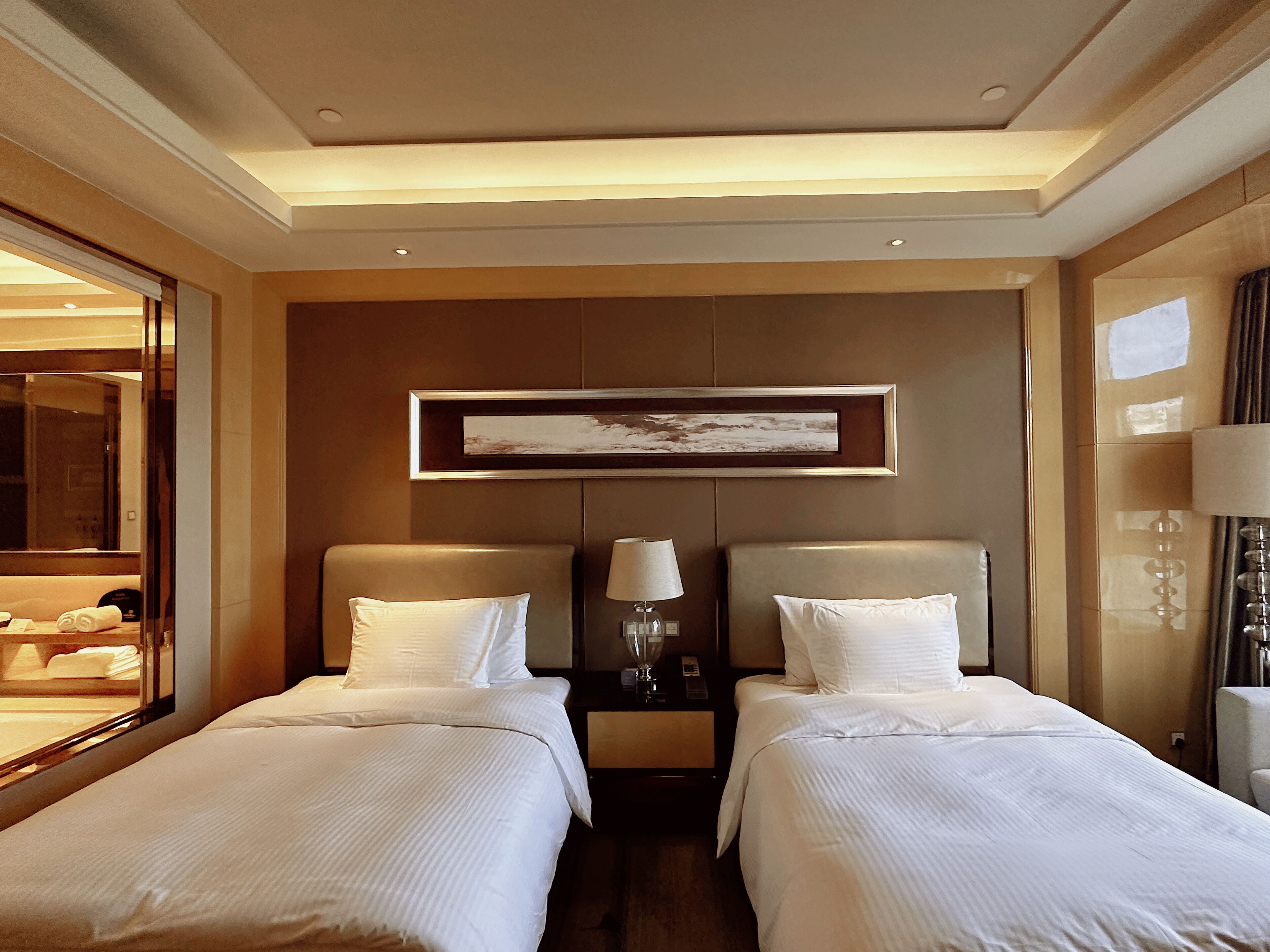 Una habitación de hotel con dos camas, un espejo grande, una obra de arte enmarcada en la pared y una mesita de noche con lámpara.