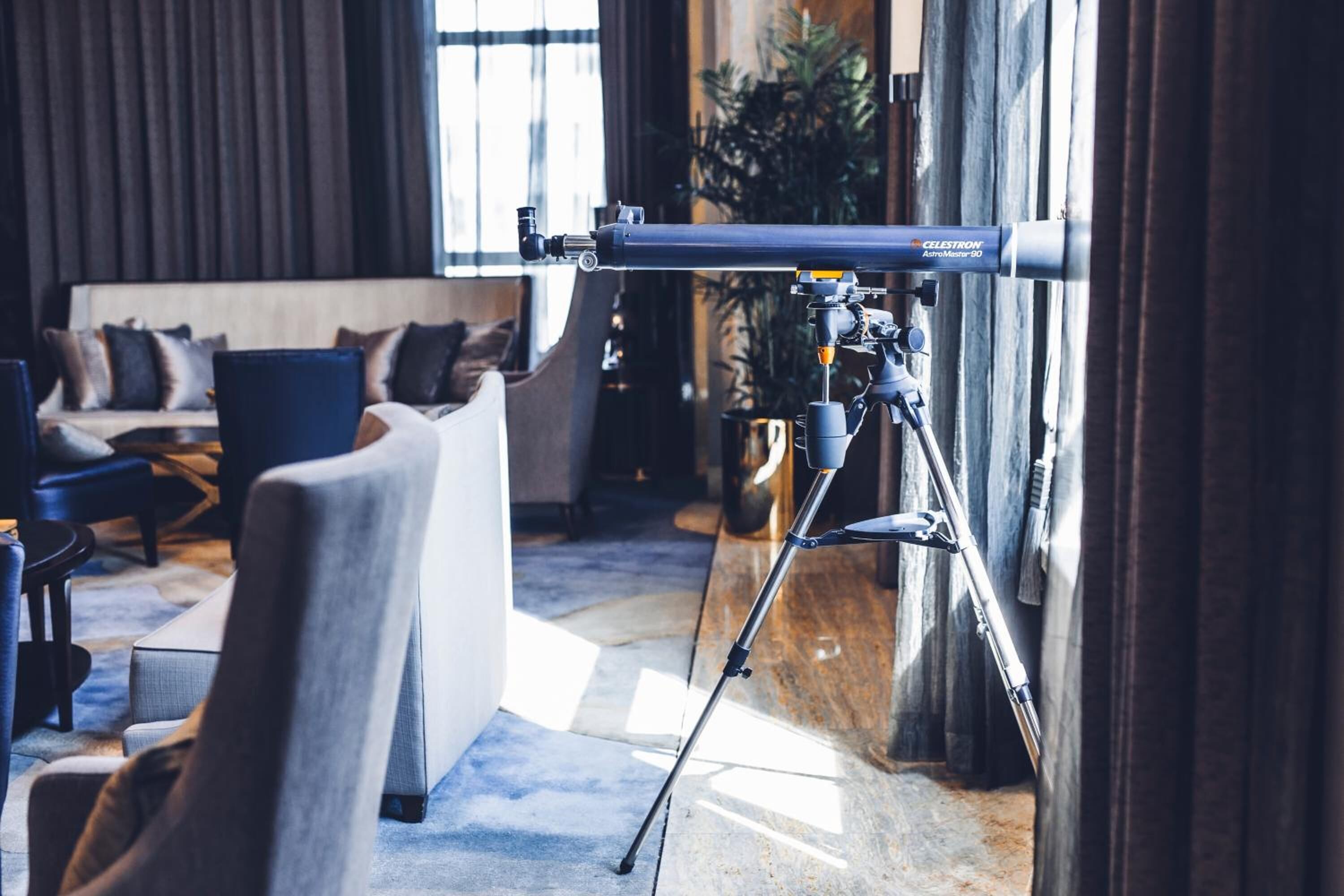 A telescope on a tripod in a room with a sofa and chairs.