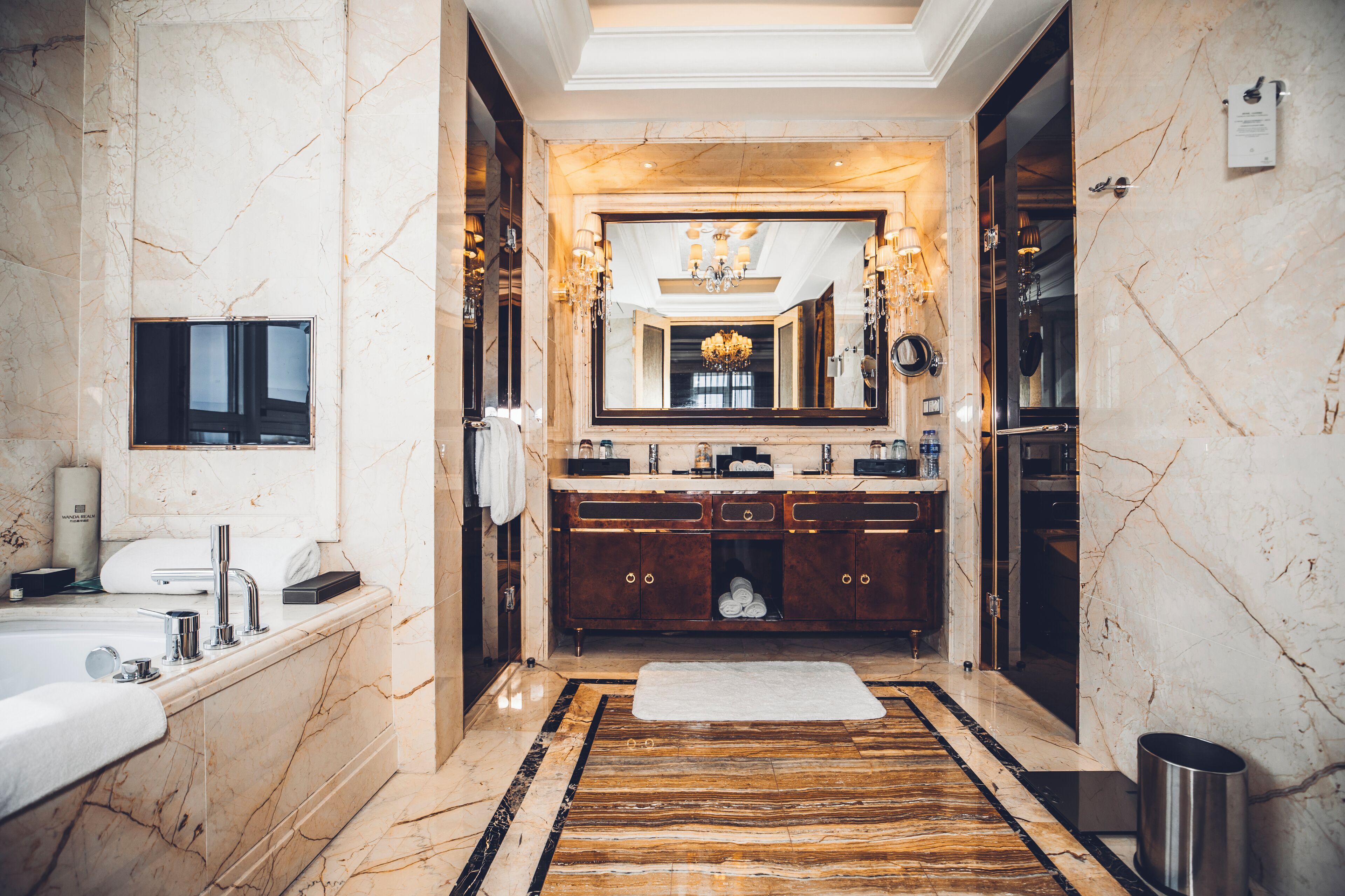 A luxurious bathroom with a marble floor, a large mirror, a bathtub, and a vanity with a sink and towel rack.