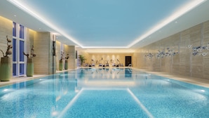 A large indoor swimming pool with clear blue water, surrounded by modern decor and seating areas. - Wanda Realm Dandong (Dandong)