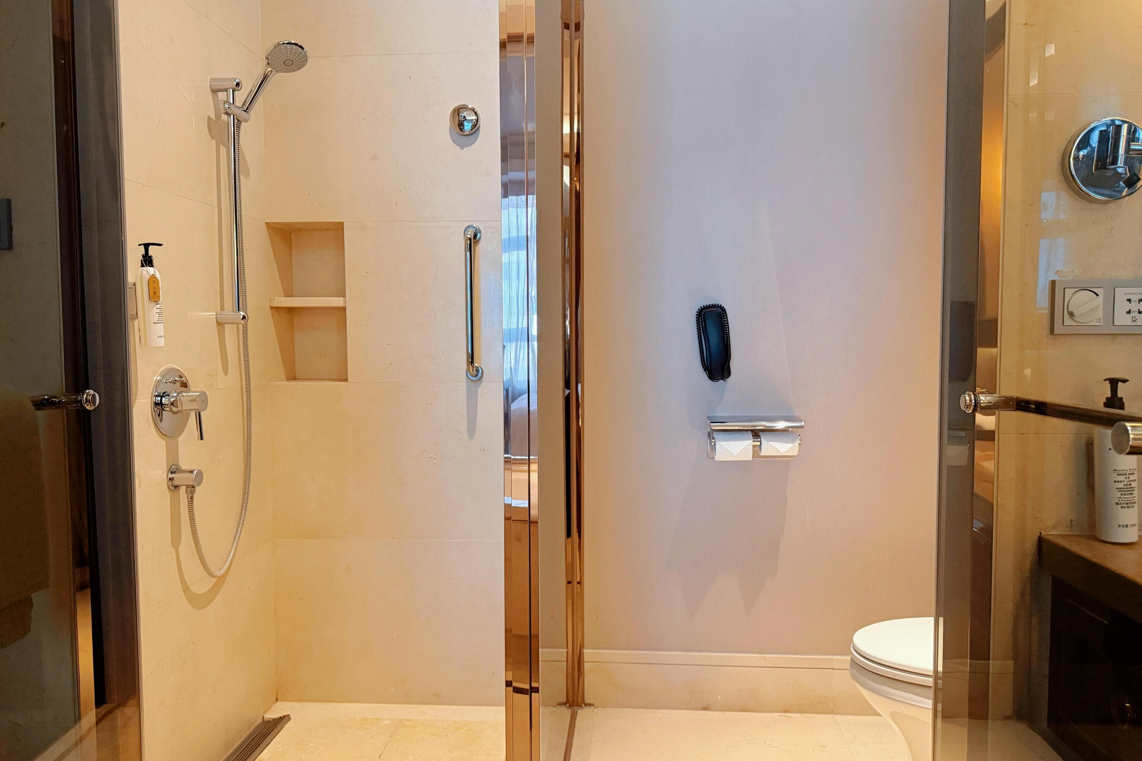 A modern bathroom with a glass-enclosed shower, a toilet, and a sink with a soap dispenser.