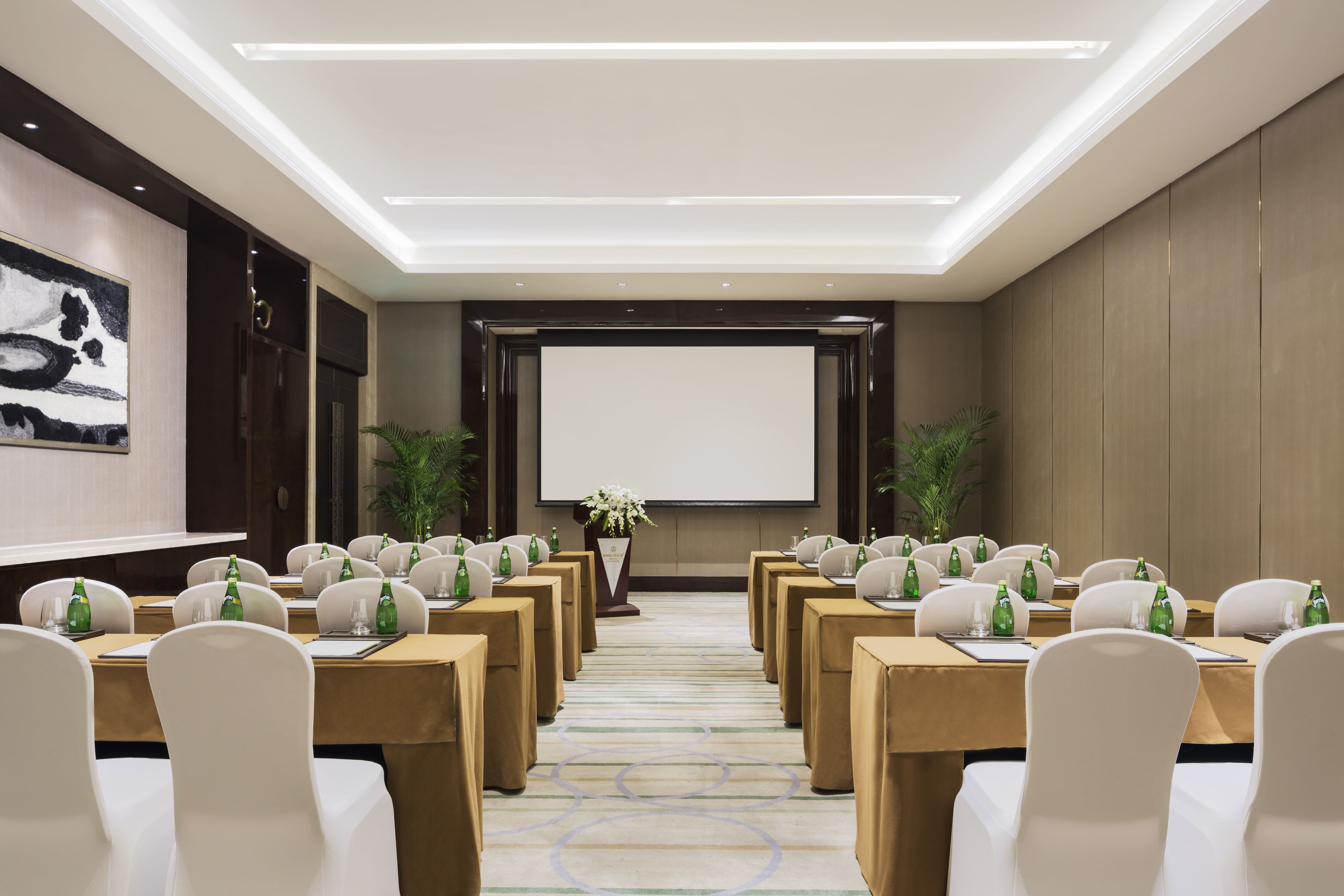 A conference room with rows of tables, chairs, and a projector screen.