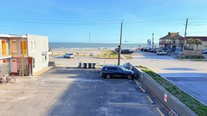 Ein Parkplatz mit Autos, ein Gebäude mit einem Balkon und ein Strand im Hintergrund.