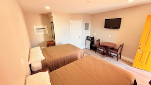 A hotel room with two beds, a desk with a chair, a television, and a door.