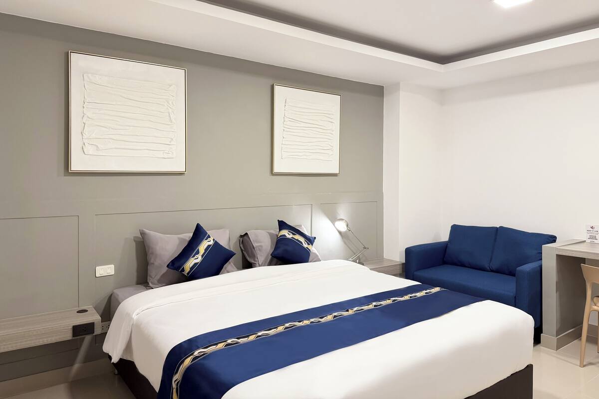 Een moderne hotelkamer met een groot bed, een blauwe bank en twee ingelijste kunstwerken aan de muur.