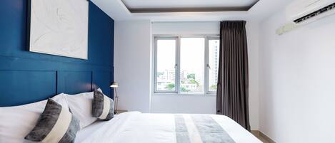 Una habitación de hotel moderna con una cama grande, vistas de la ciudad a través de una ventana y un equipo de aire acondicionado en la pared.