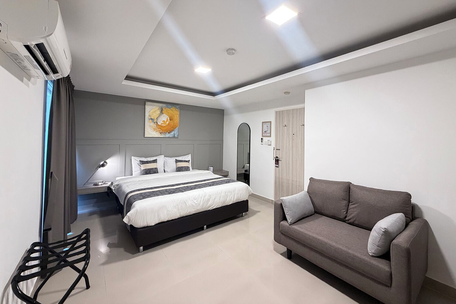 Ett modernt hotellrum med en stor säng, en soffa, ett skrivbord och en luftkonditioneringsanläggning.