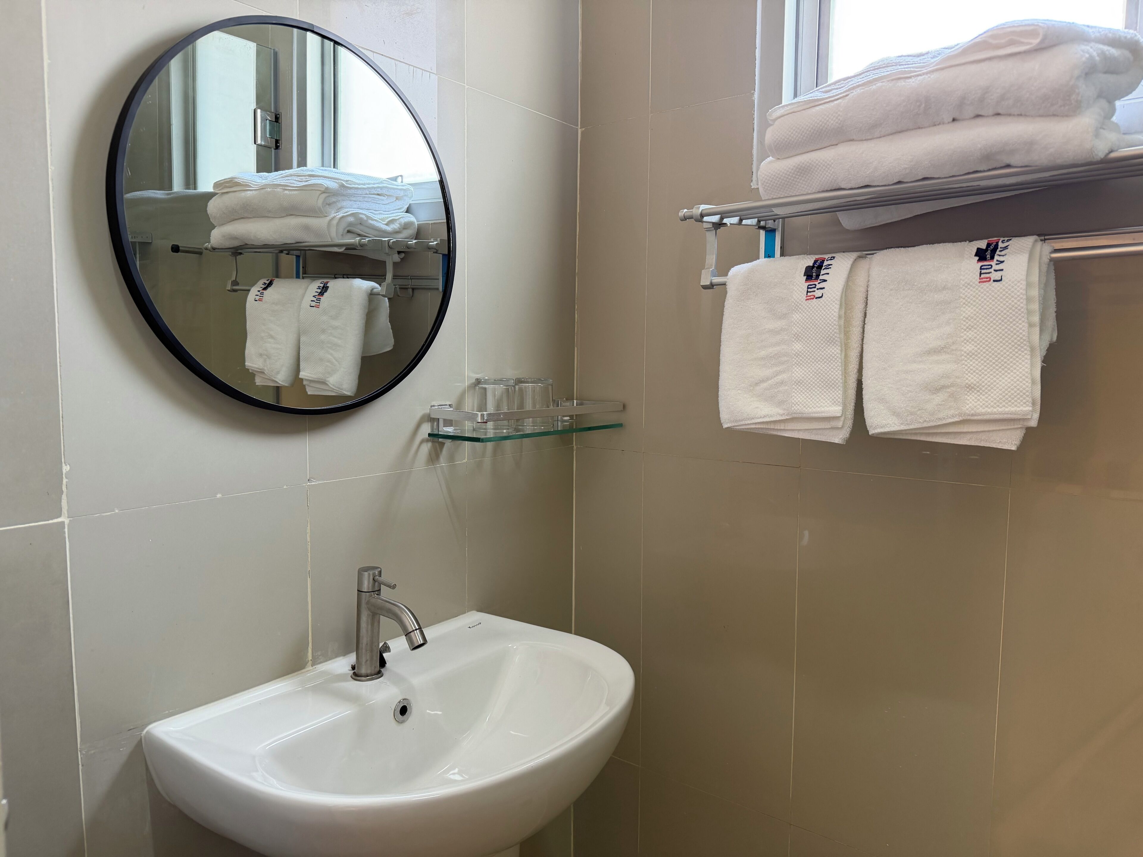 A bathroom with a round mirror, a sink, and a towel rack with folded towels.