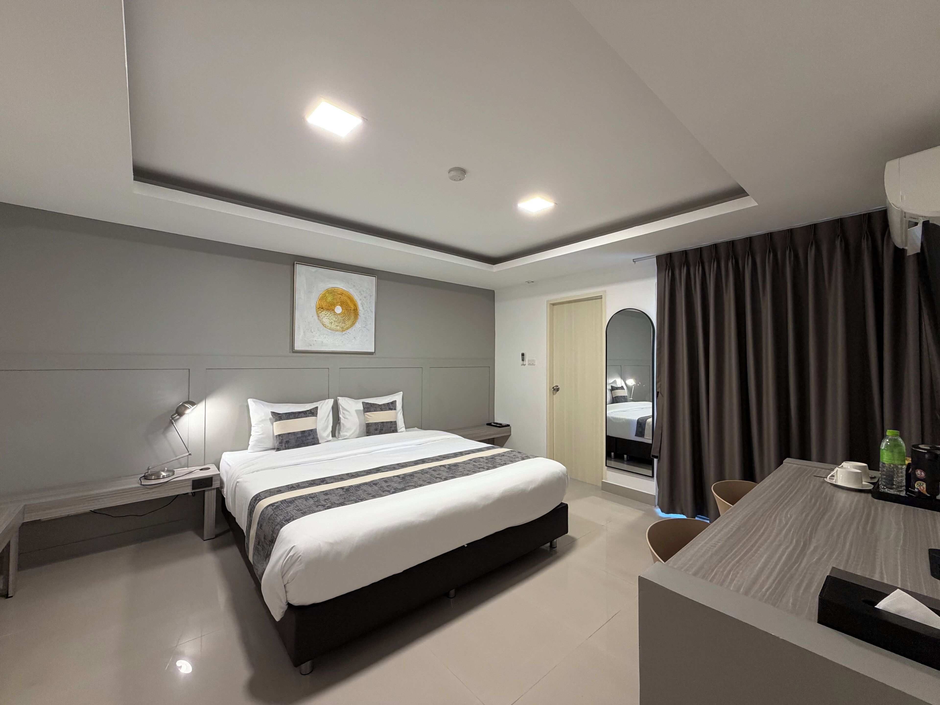 A modern hotel room with a bed, bedside table, lamp, and a dining area with a table and chairs.