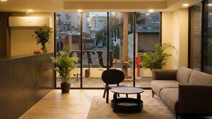 Um interior moderno com sofá, uma mesinha, cadeiras, um vaso de planta e uma janela ampla com vista para edifícios.
