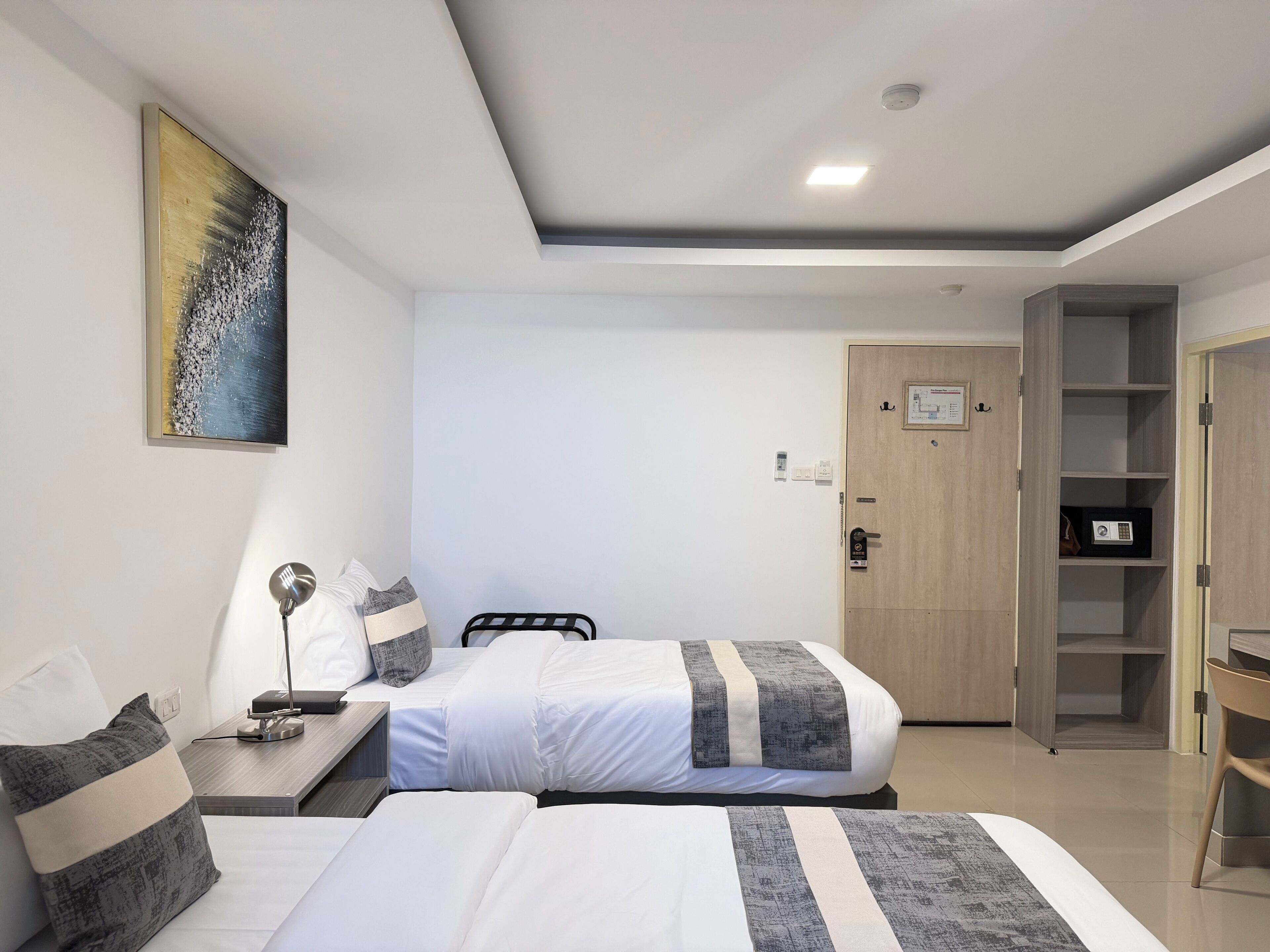 A hotel room with two beds, a desk, a chair, a wardrobe, and a painting on the wall.