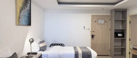 A hotel room with two beds, a desk, a chair, a wardrobe, and a painting on the wall.