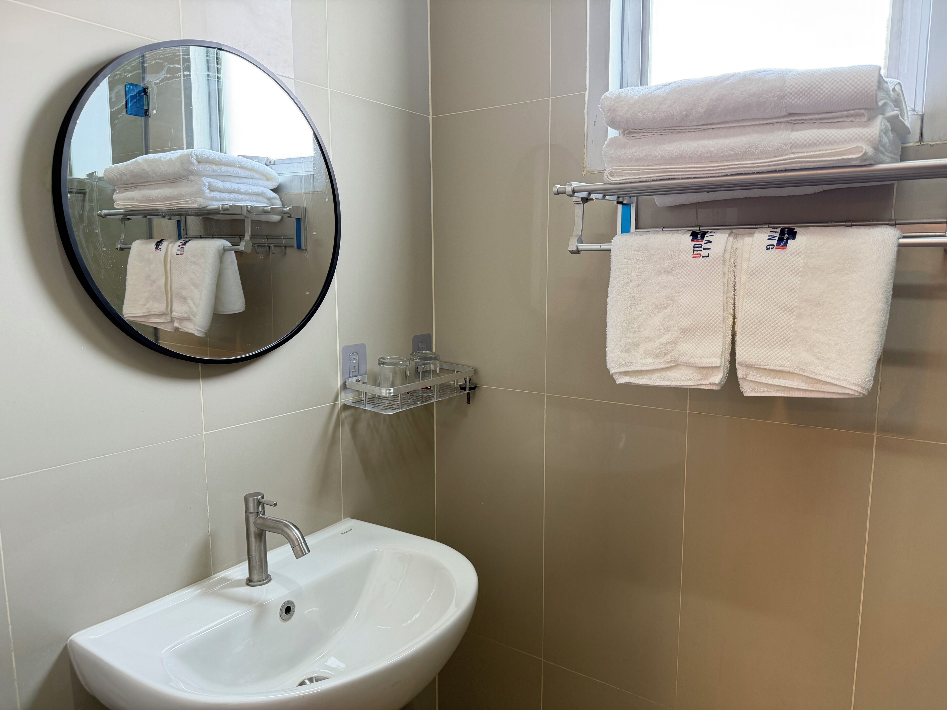 Un baño con un espejo redondo, un lavabo y un toallero con toallas dobladas.