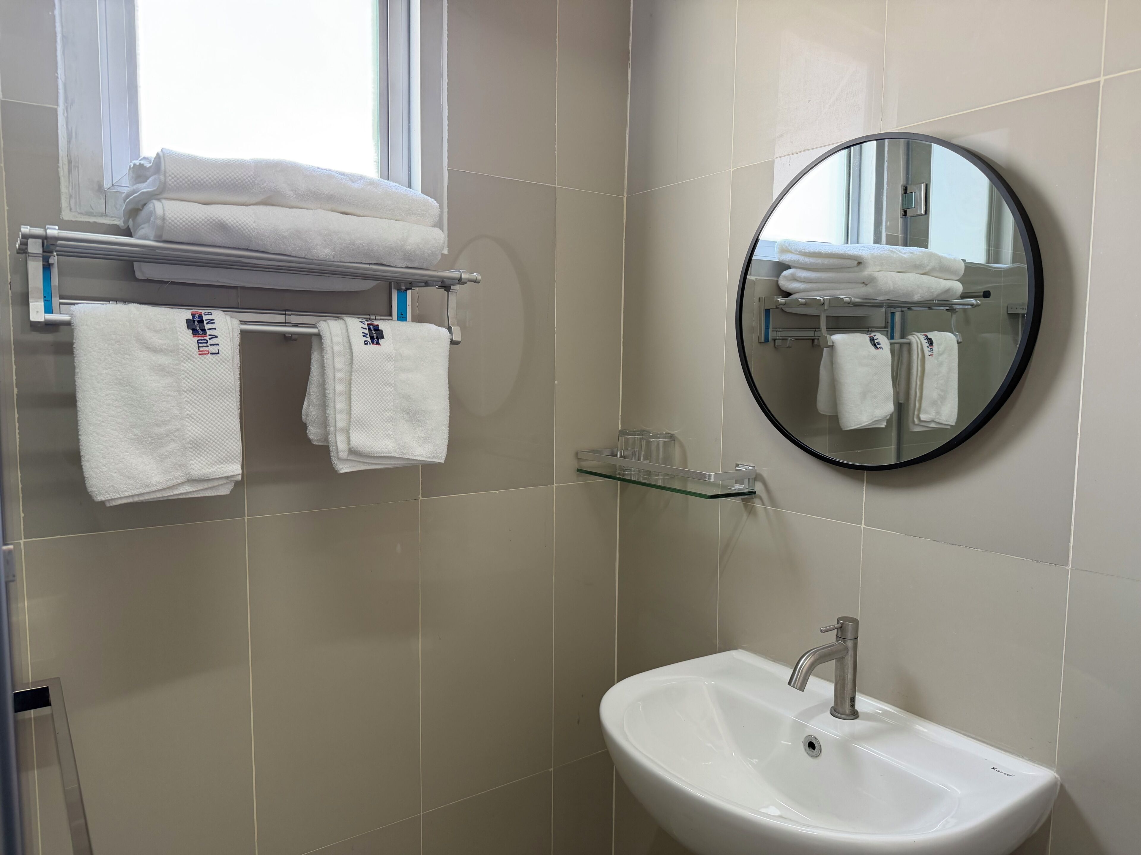Een badkamer met een wastafel, spiegel, handdoekhouder en een raam.