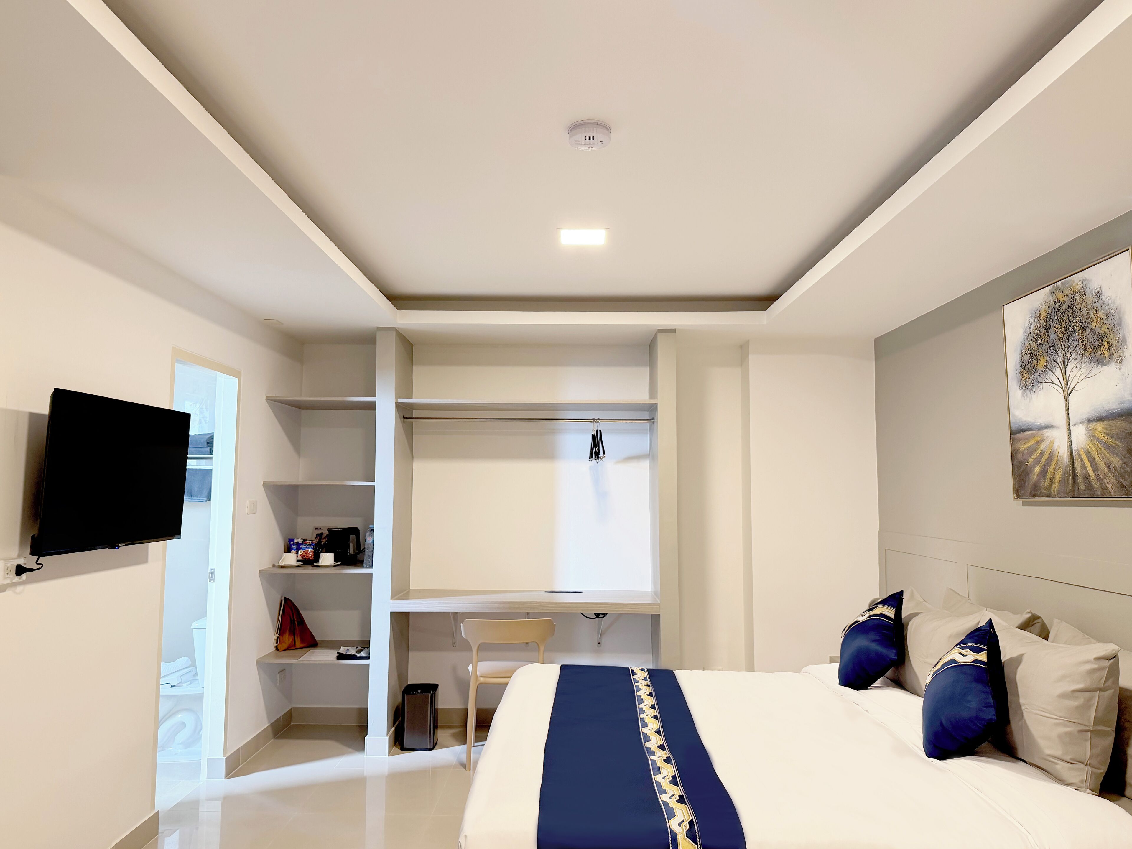 Une chambre d’hôtel moderne équipée d’un lit, d’une télévision à écran plat, d’un bureau et d’un dressing.