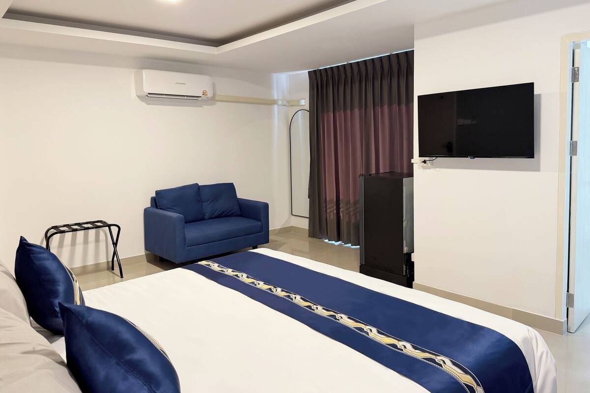 Een hotelkamer met een bed, een blauwe bank, een televisie en een airconditioner.