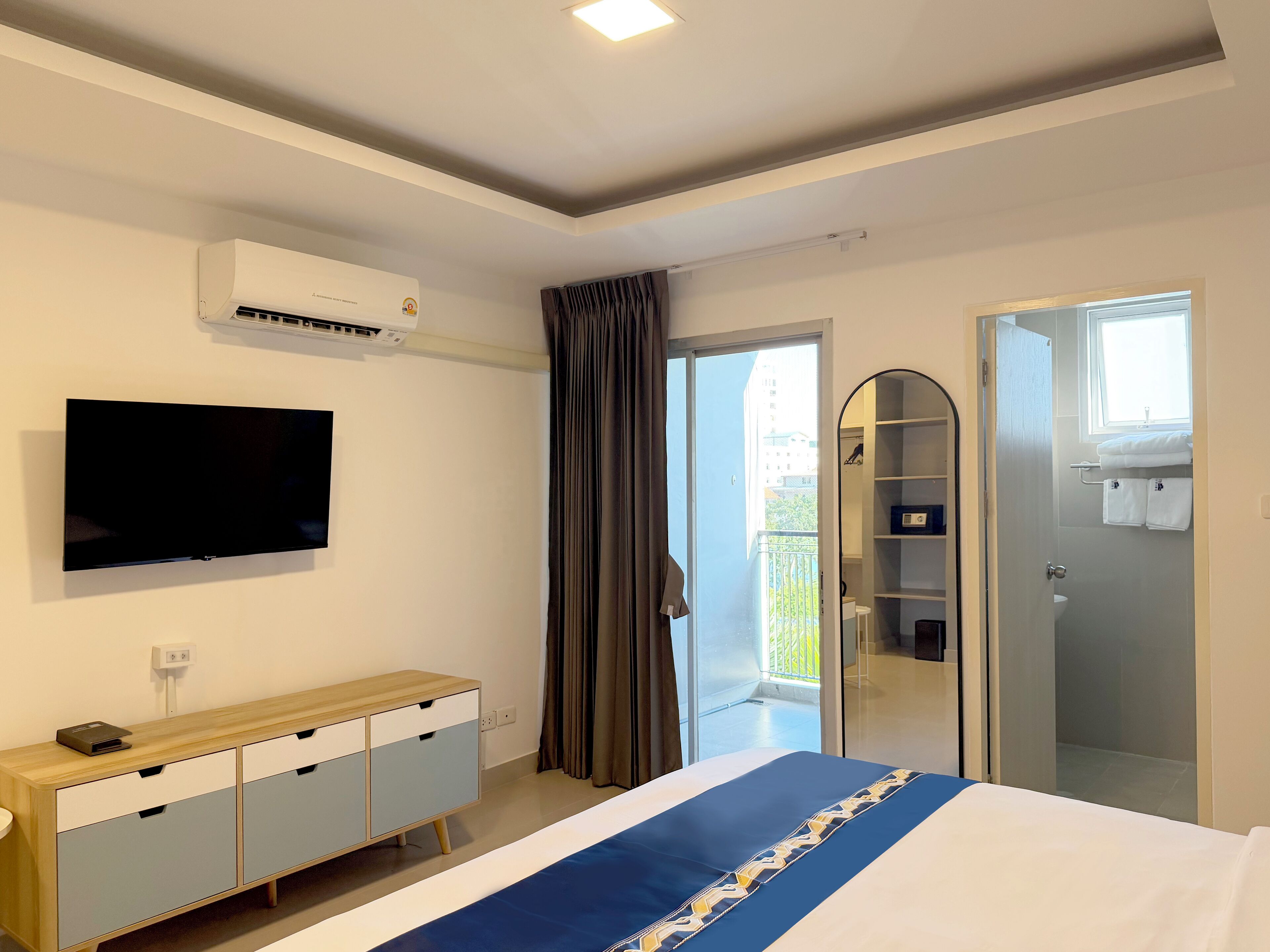 A hotel room with a bed, a TV, a wardrobe, a mirror, and a balcony with curtains.