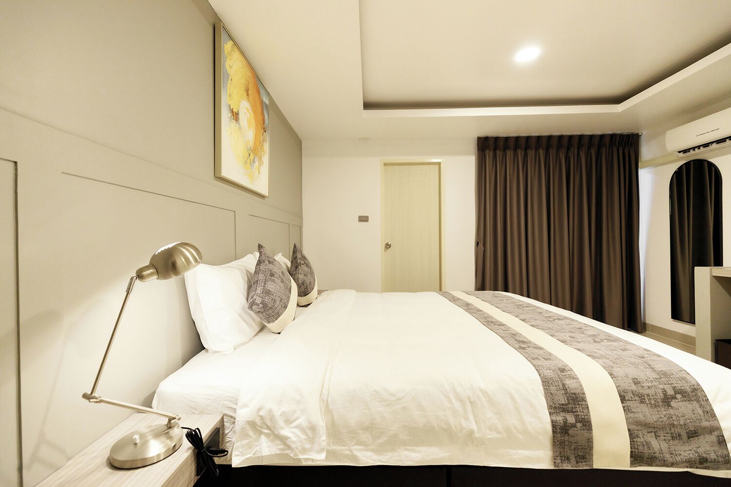 A hotel room with a large bed, a bedside lamp, a painting on the wall, and a door with curtains.