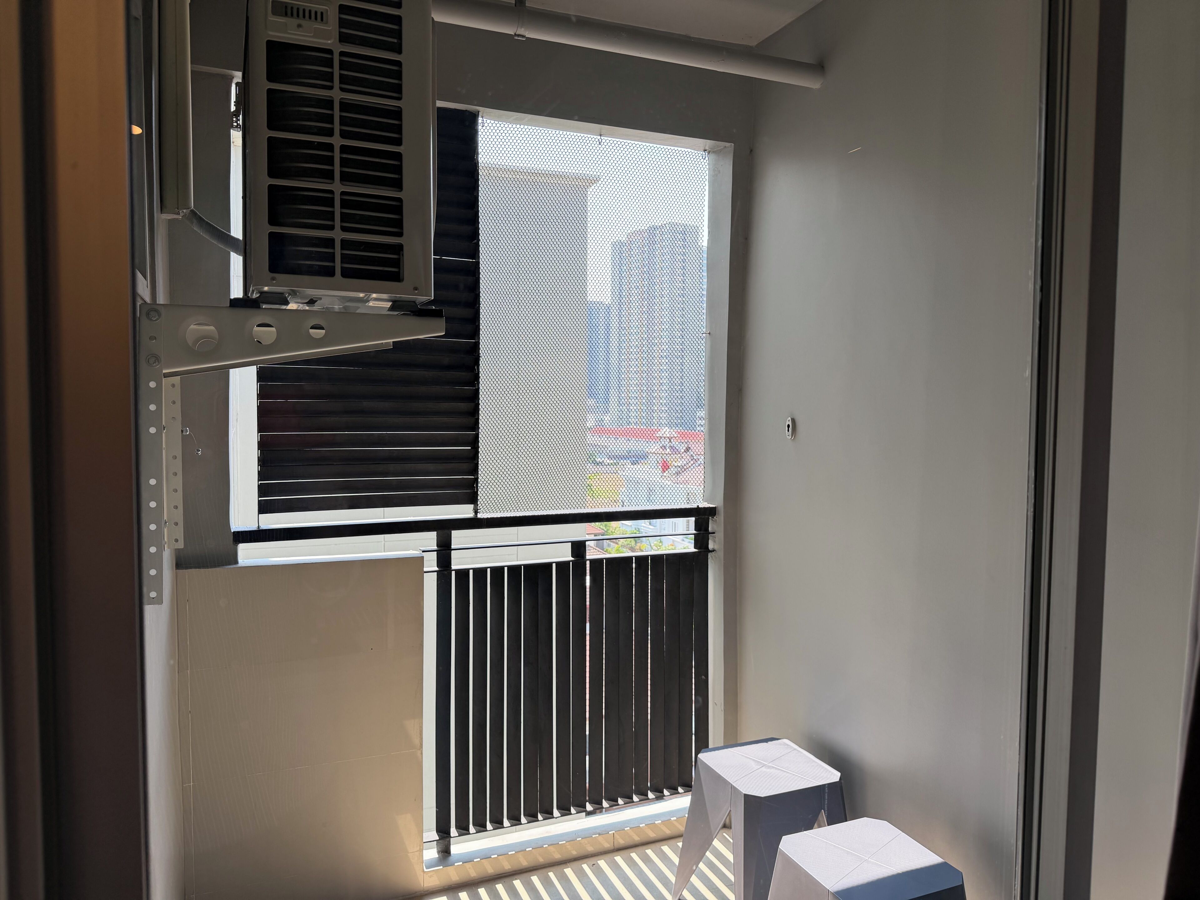 A room with a window, a metal air conditioning unit, a small table, and a barred window.