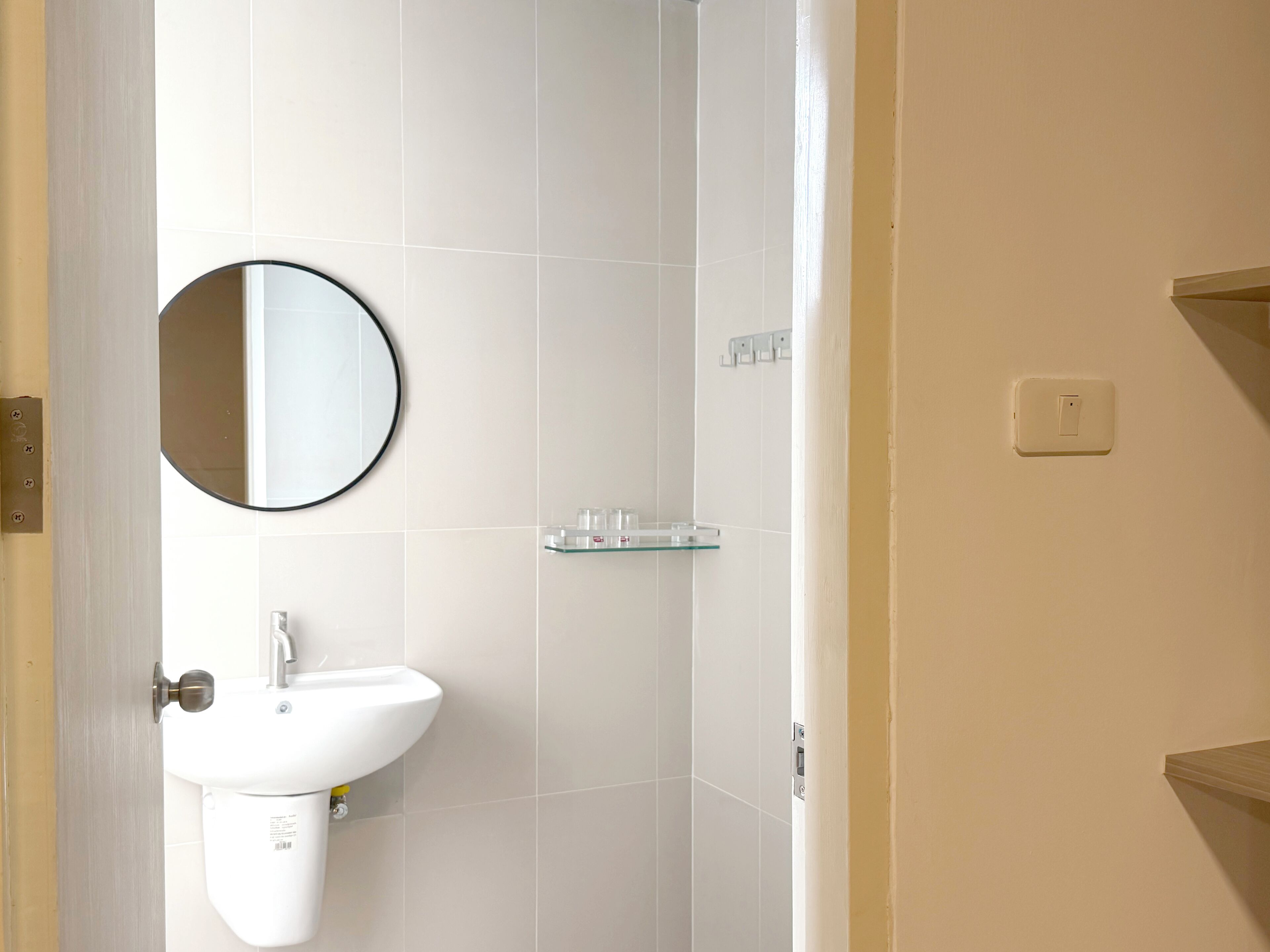 A bathroom with a white sink, a round mirror, and a glass shelf.