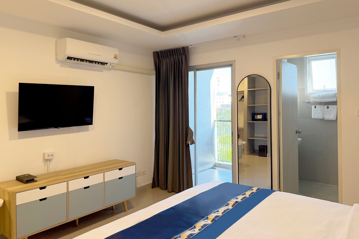 Une chambre d’hôtel équipée d’un lit, d’une télévision, d’une armoire, d’un miroir et d’un balcon avec des rideaux.