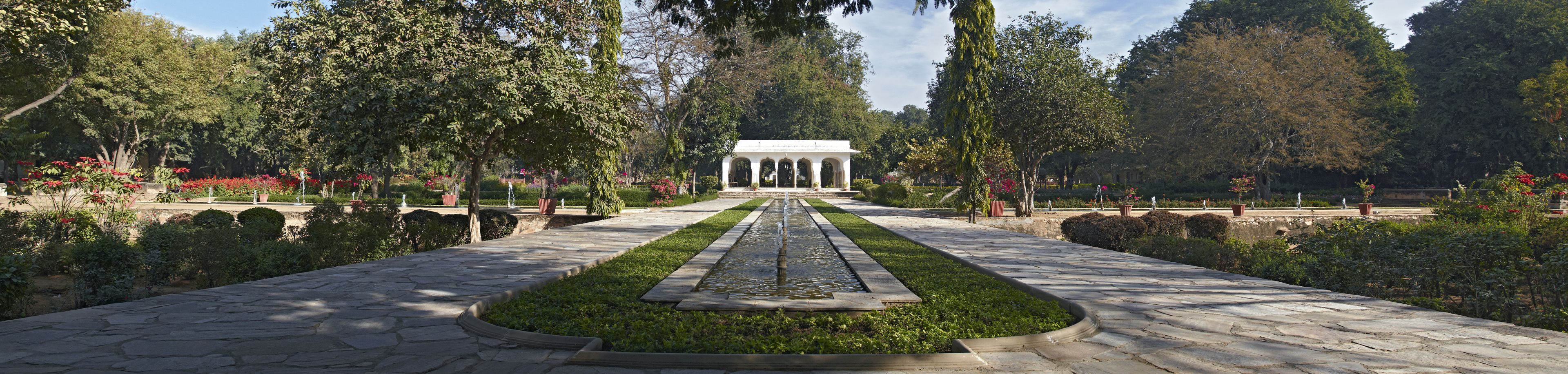 Un jardín simétrico con un elemento acuático central, senderos y un pabellón blanco.