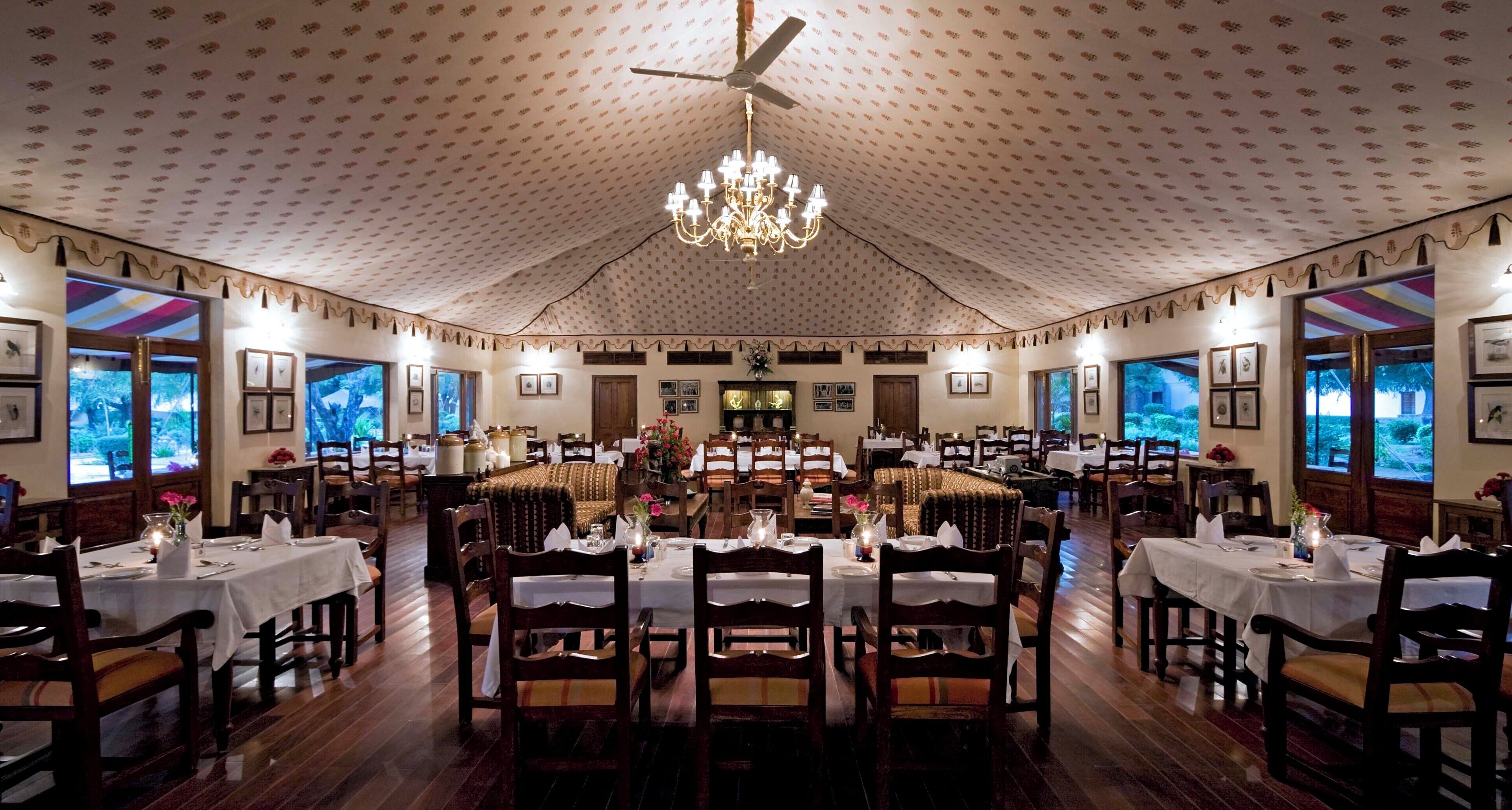 A large dining hall with multiple tables, chandeliers, and framed pictures on the walls.