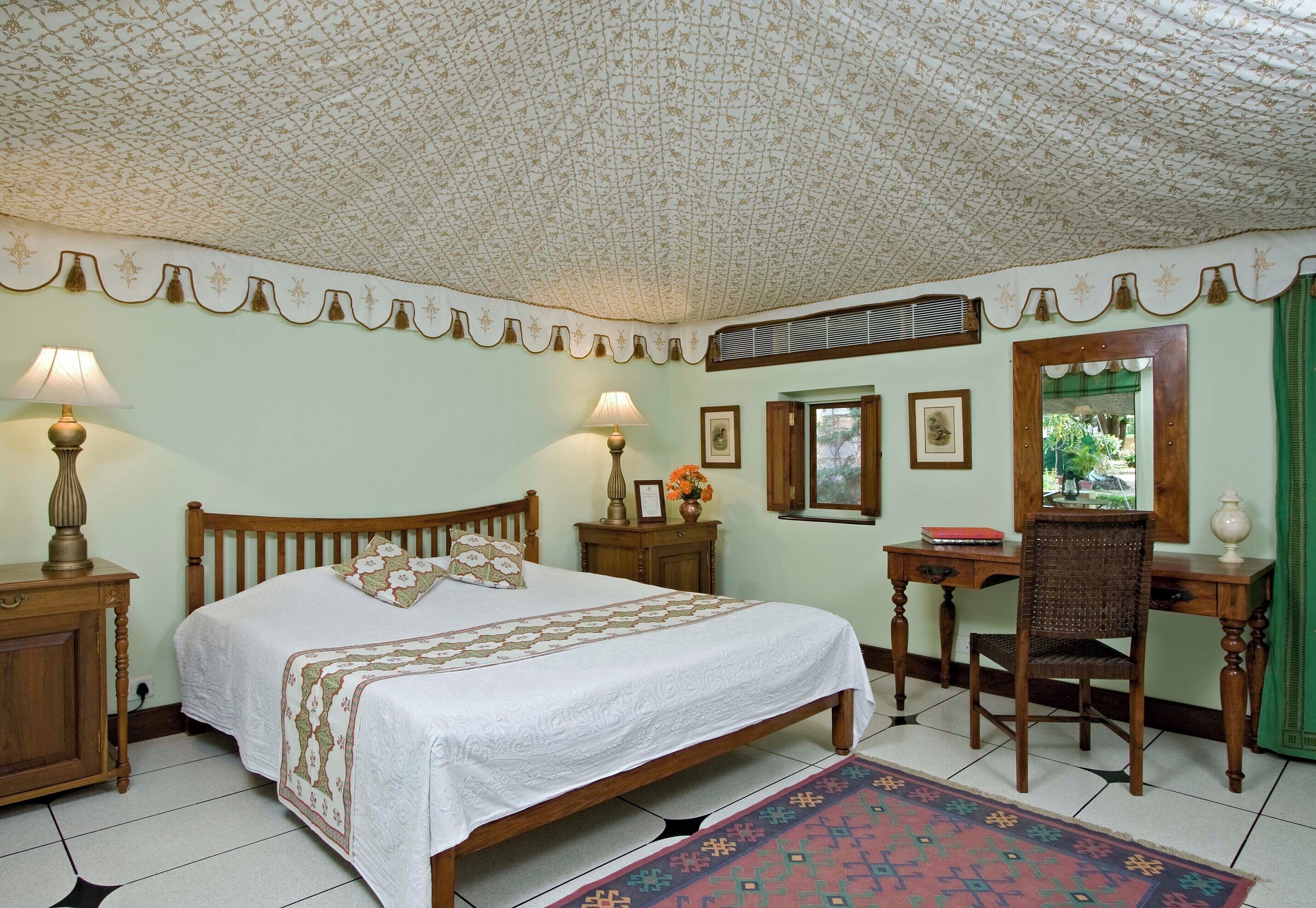 A bedroom with a bed, bedside lamps, a desk, a chair, and a mirror.