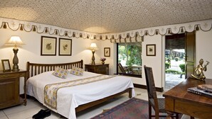 Ein Schlafzimmer mit einem großen Bett, zwei Nachttischen mit Lampen, einem Holzstuhl, einem Schreibtisch mit einer Statue und gerahmten Bildern an der Wand.