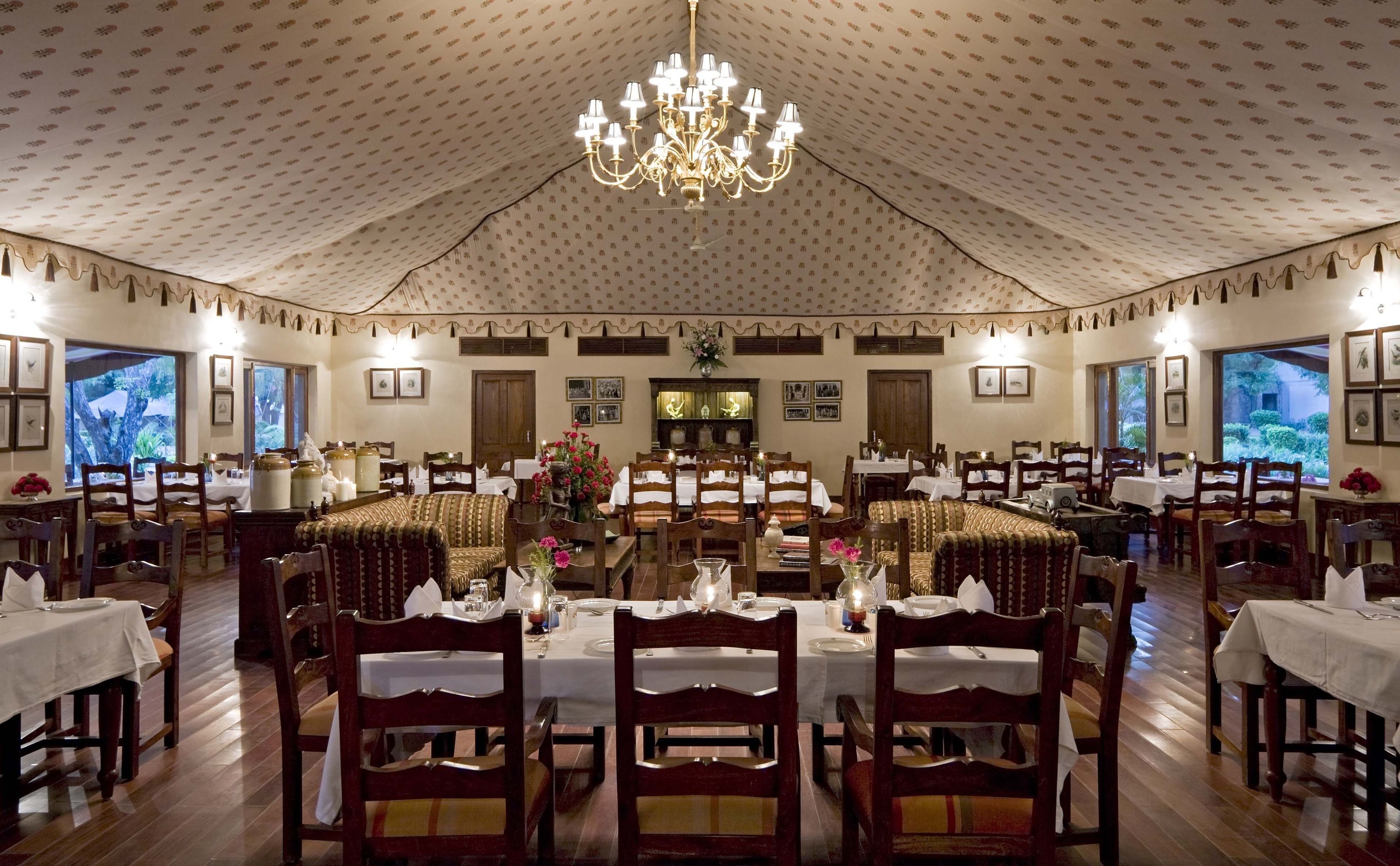 Un amplio comedor con varias mesas y sillas, un candelabro central y cuadros en las paredes.