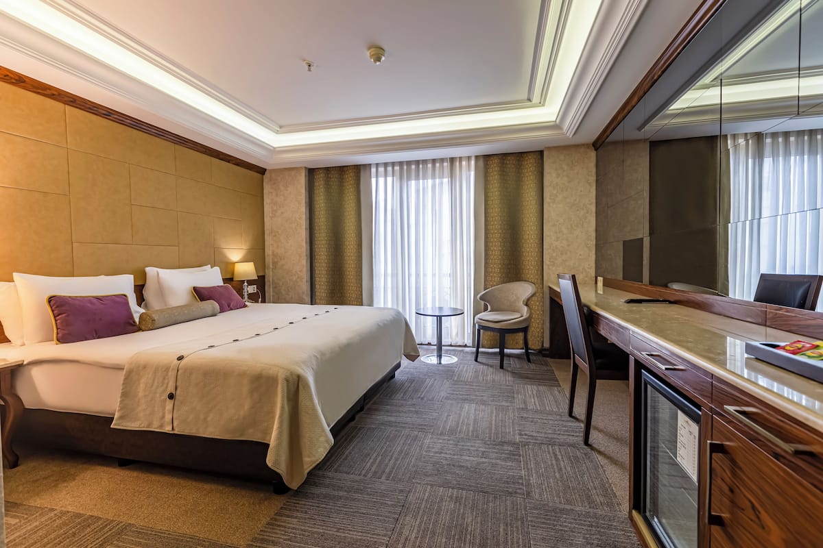 A hotel room with a bed, a desk, a chair, a small table, and a television.