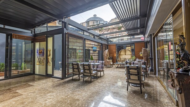 An indoor-outdoor dining area with glass walls, outdoor seating, and a view of a historic building. - Euro Stars Hotel Old City (Istanbul)