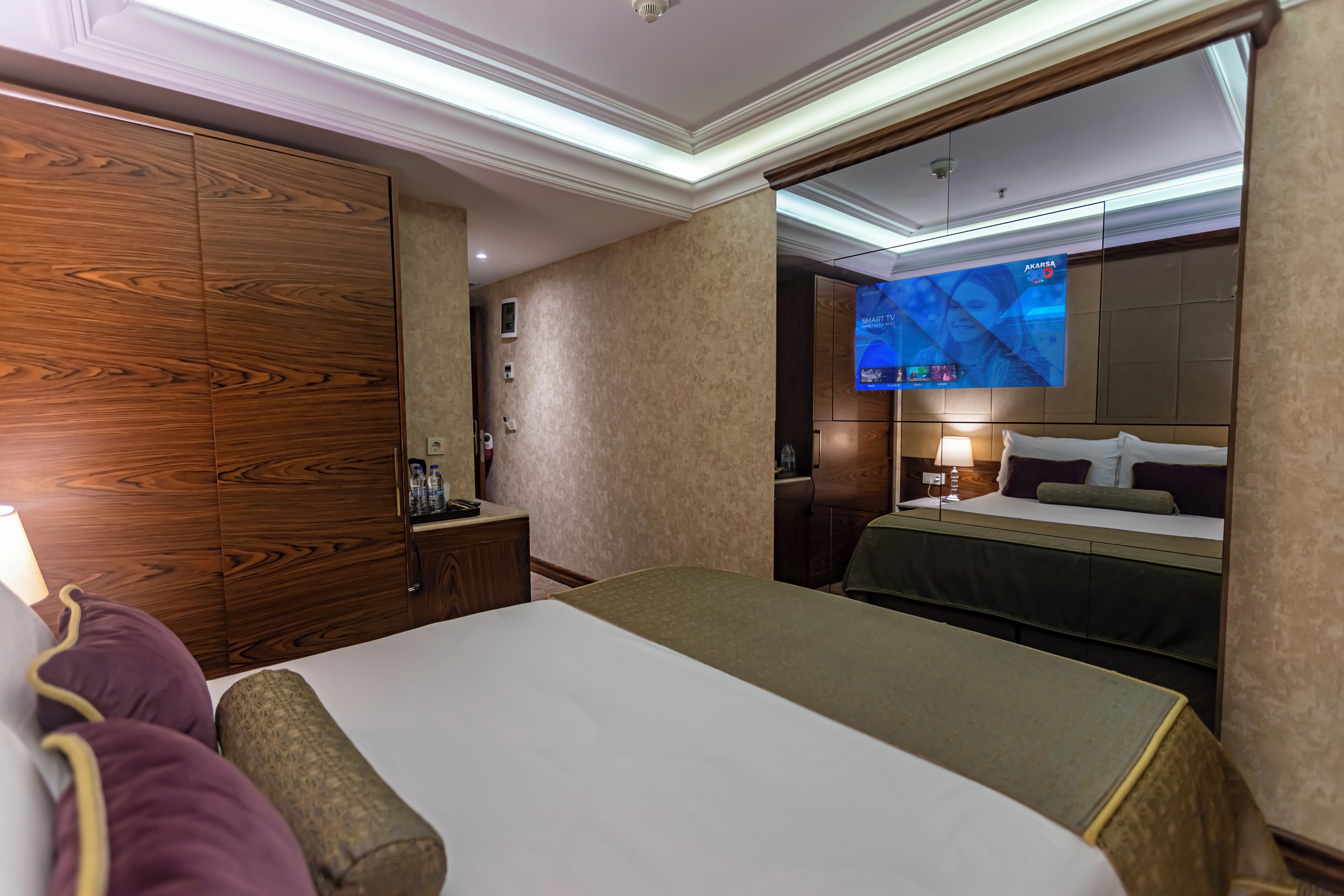 A hotel room with a large bed, a wooden wardrobe, a television, and a desk with a lamp.