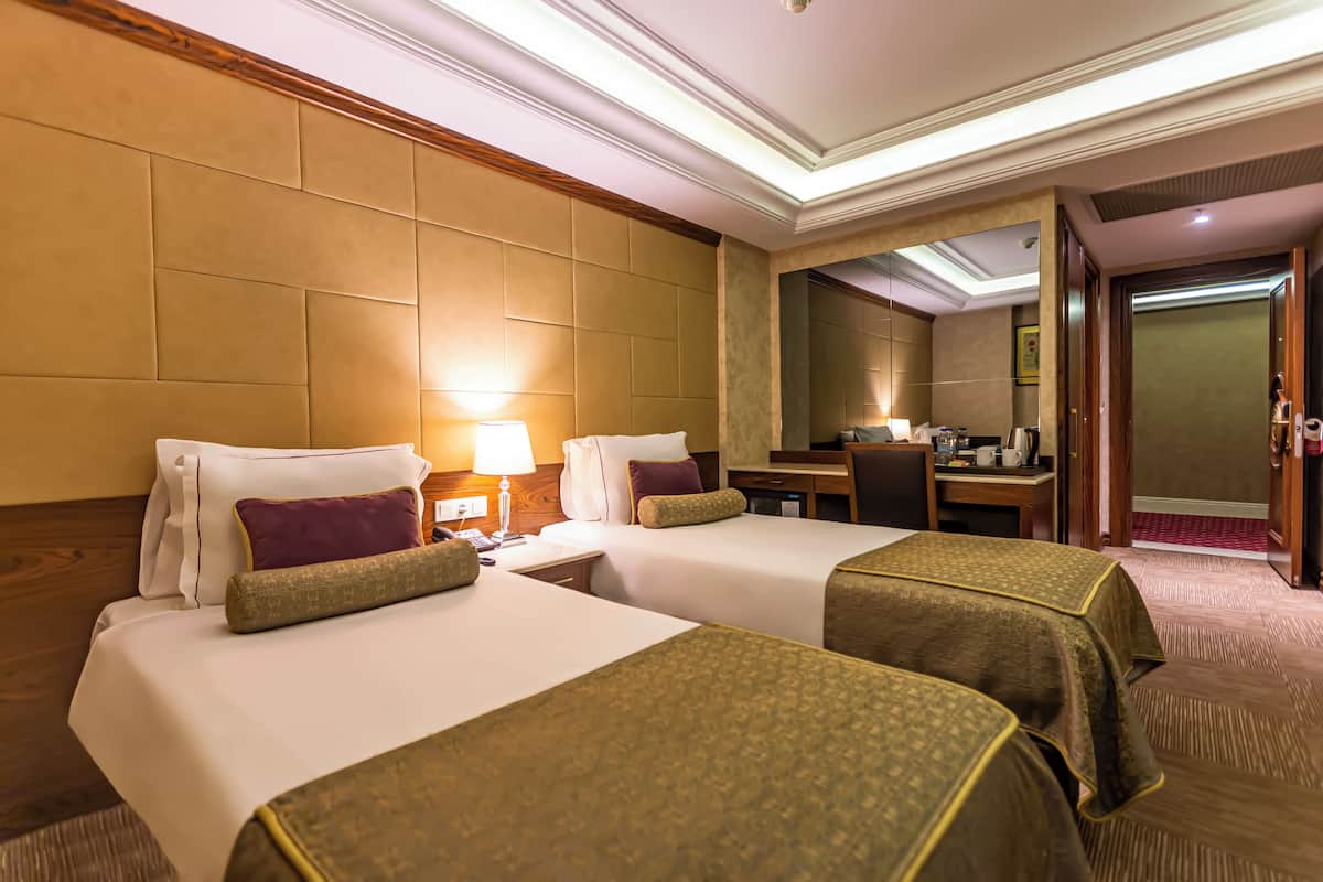 A hotel room with two beds, a desk, a chair, a lamp, and a mirror.