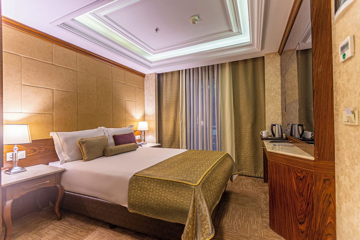 A hotel room with a bed, bedside tables, a desk, a mirror, curtains, and a wooden cabinet.