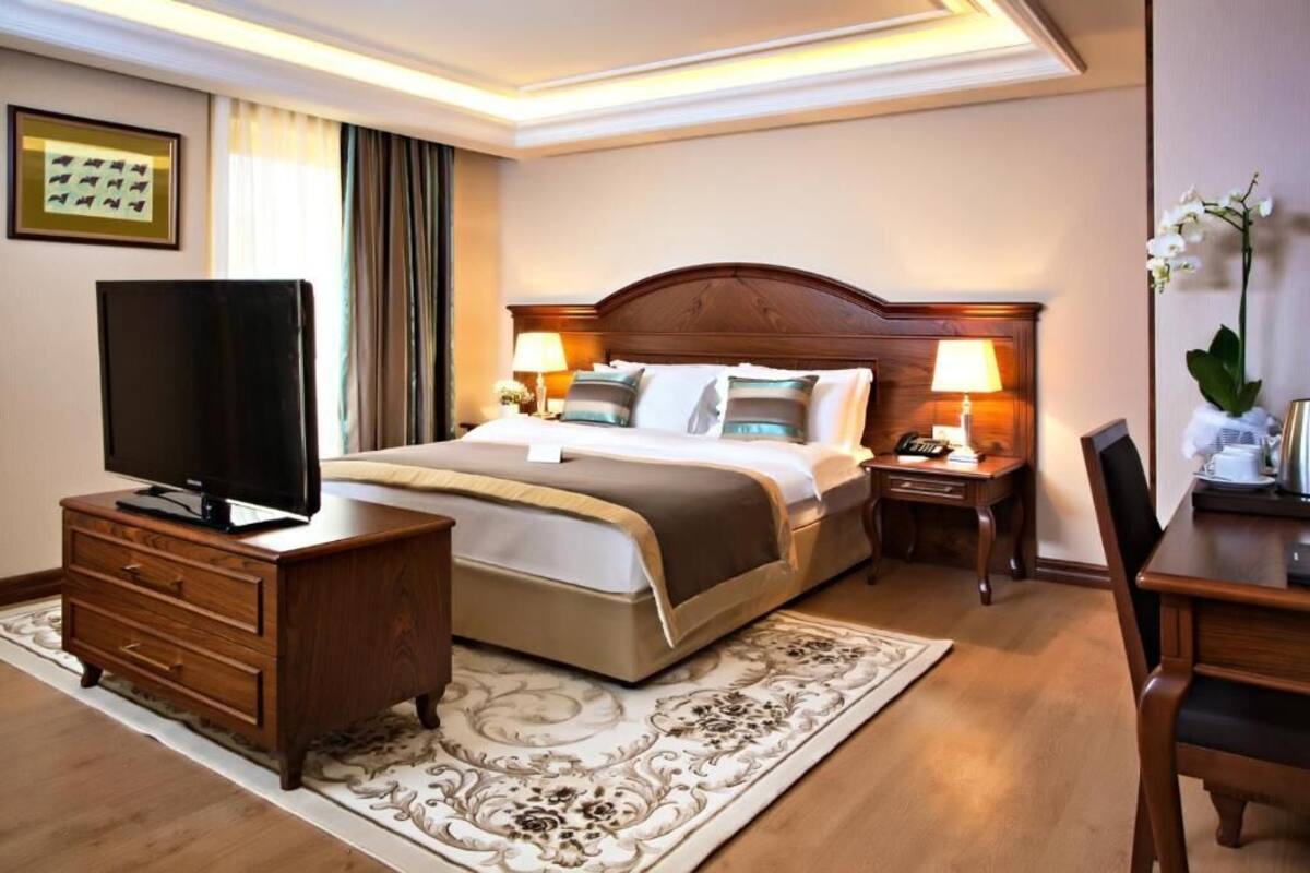 A hotel room with a bed, a TV, a desk, a chair, and a lamp.