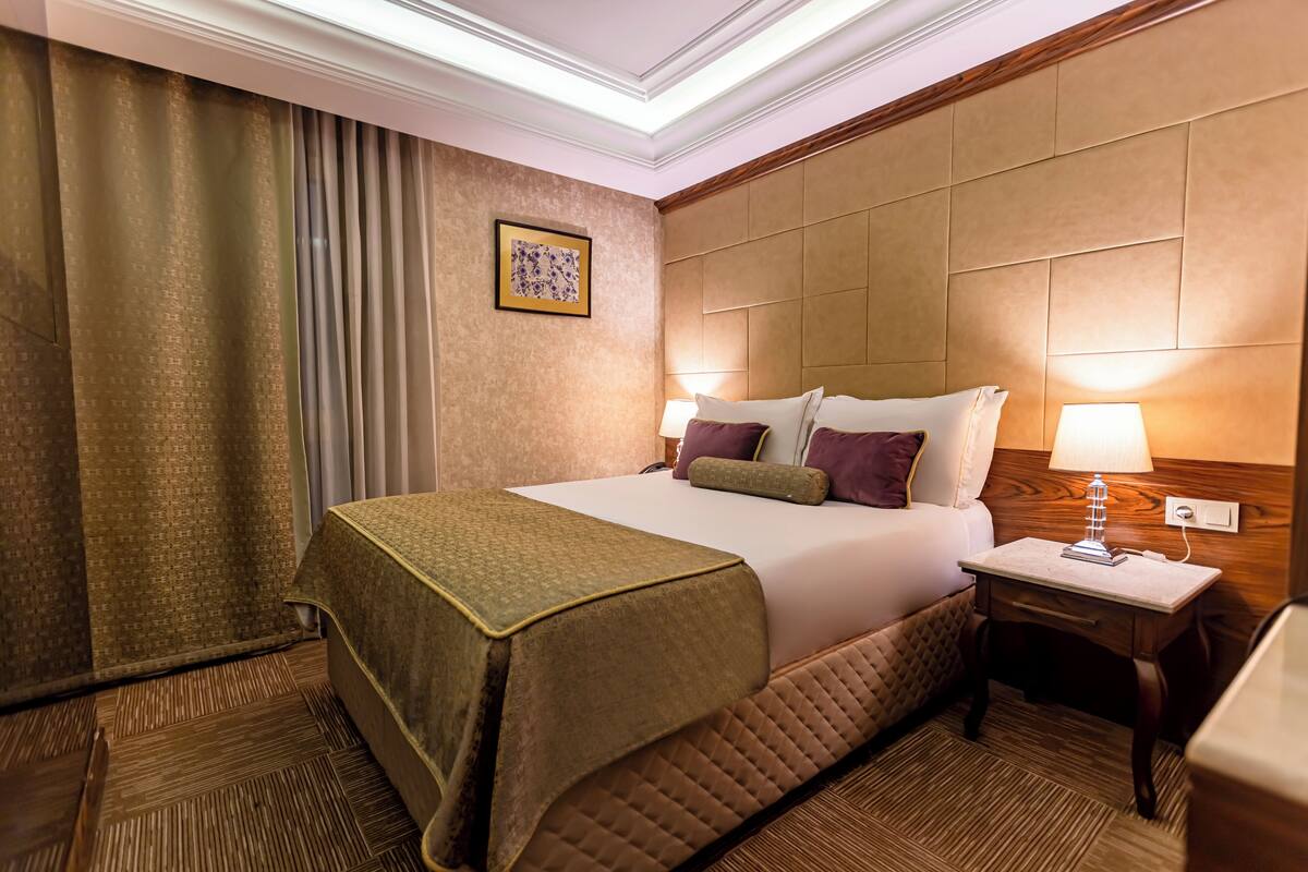 A hotel room with a bed, bedside table, lamp, and a picture on the wall.