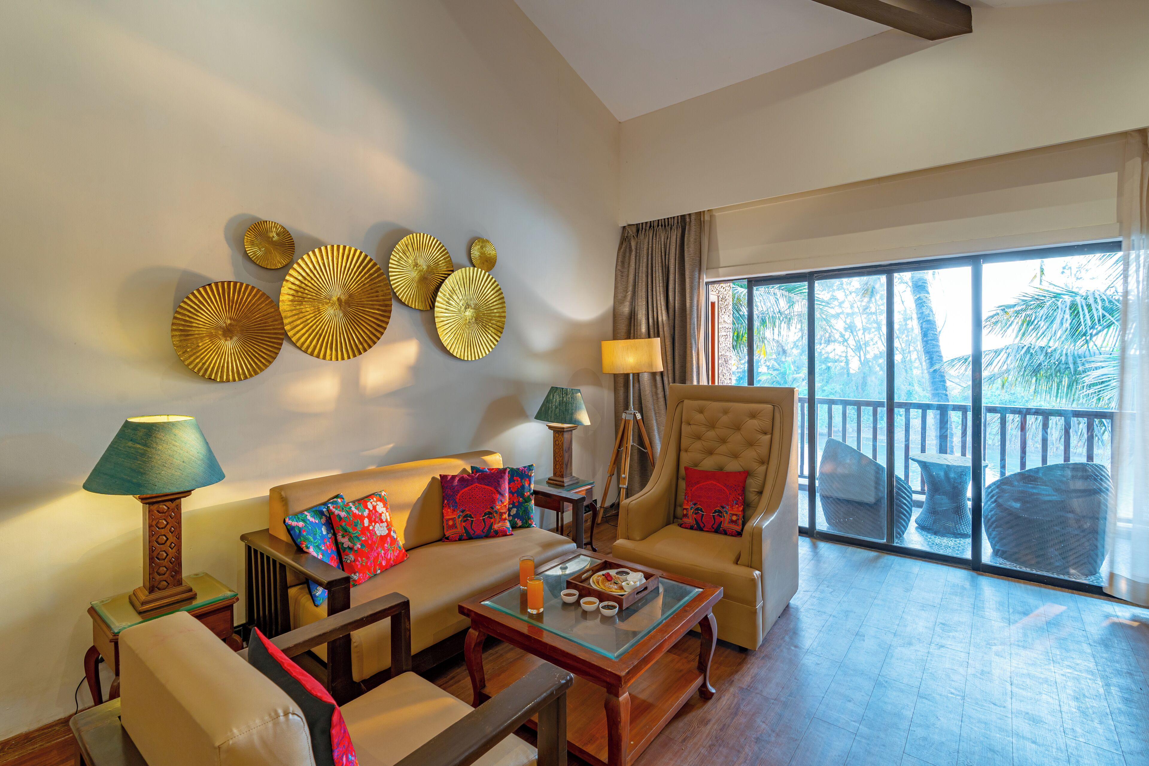 A spacious living area with a sofa, armchairs, and a coffee table. There are decorative wall pieces and a view of palm trees through large windows.