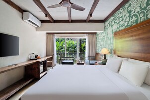 Habitación de hotel con una cama grande, un televisor de pantalla plana, un escritorio con lámpara y vistas a zonas verdes por la ventana.