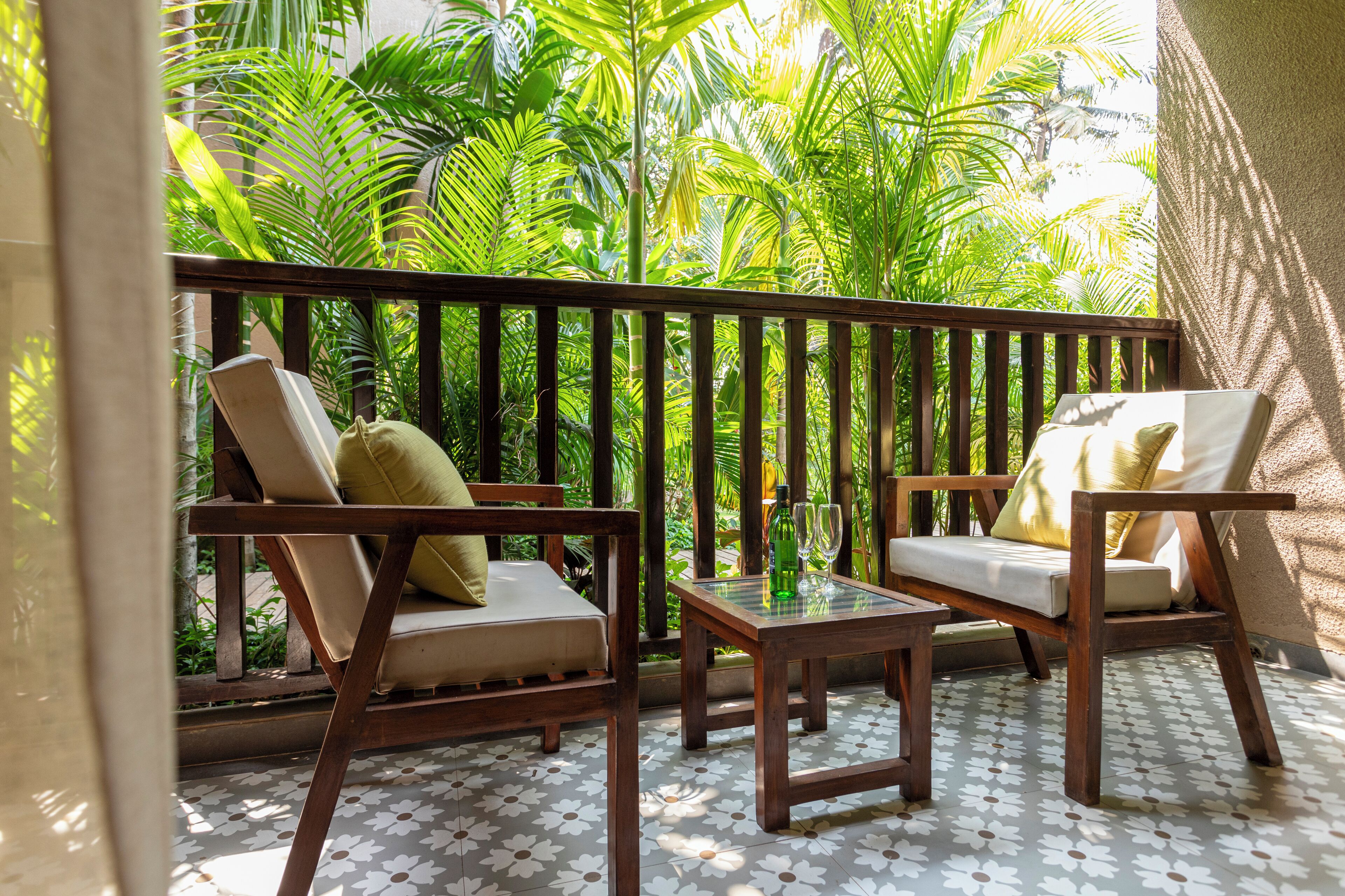 A balcony with two wooden chairs and a small table, surrounded by lush green foliage.
