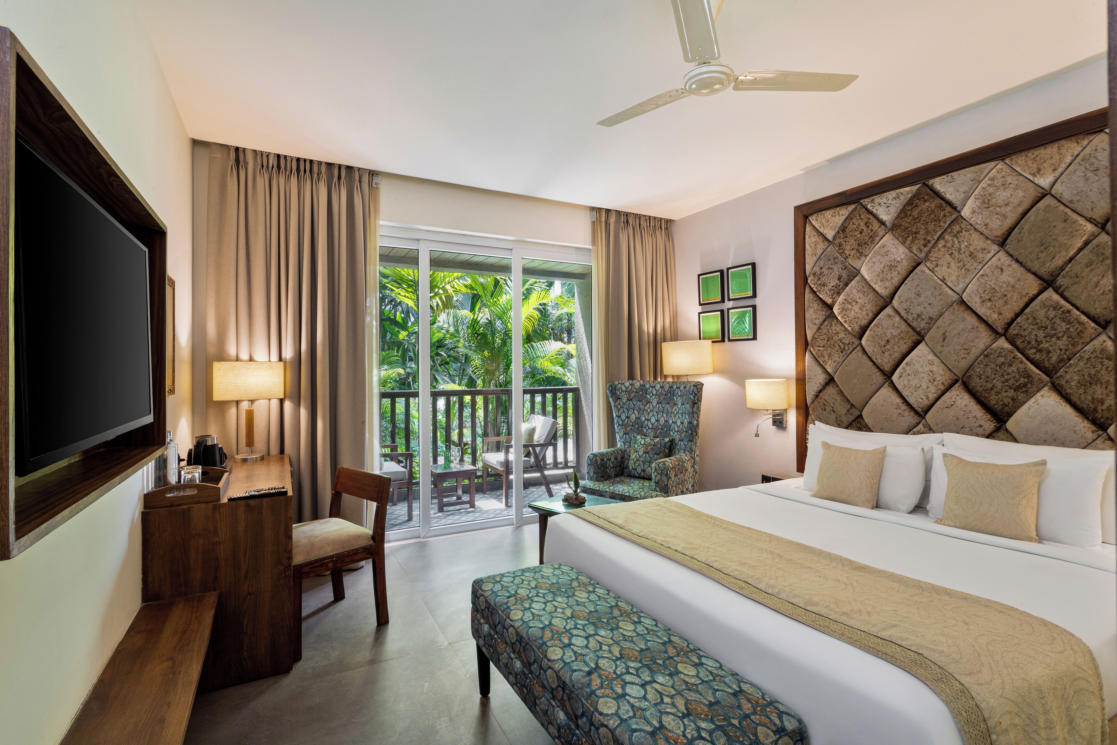A hotel room with a bed, a desk, a chair, a TV, and a balcony with curtains.