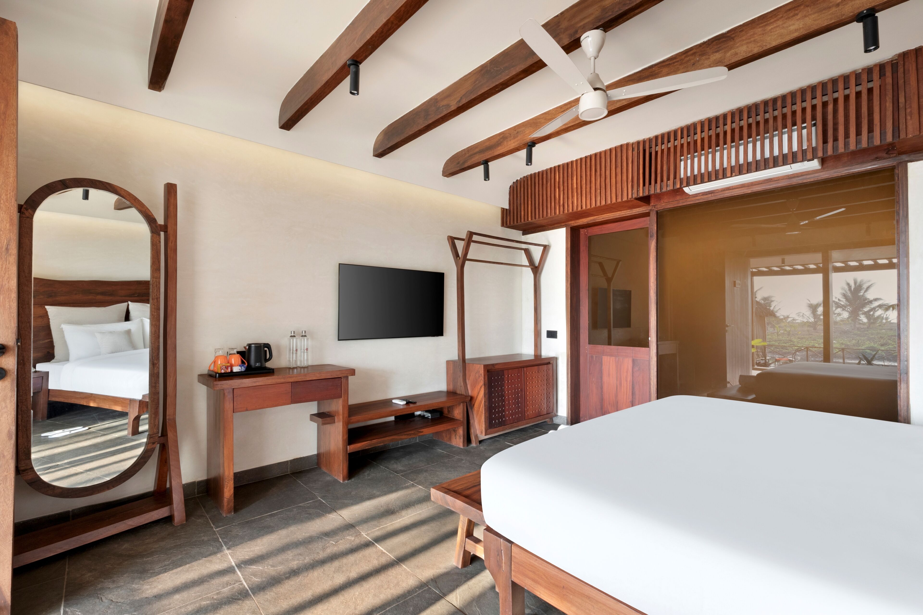 Habitación de hotel con cama, escritorio, televisor, ventilador de techo y una ventana grande.