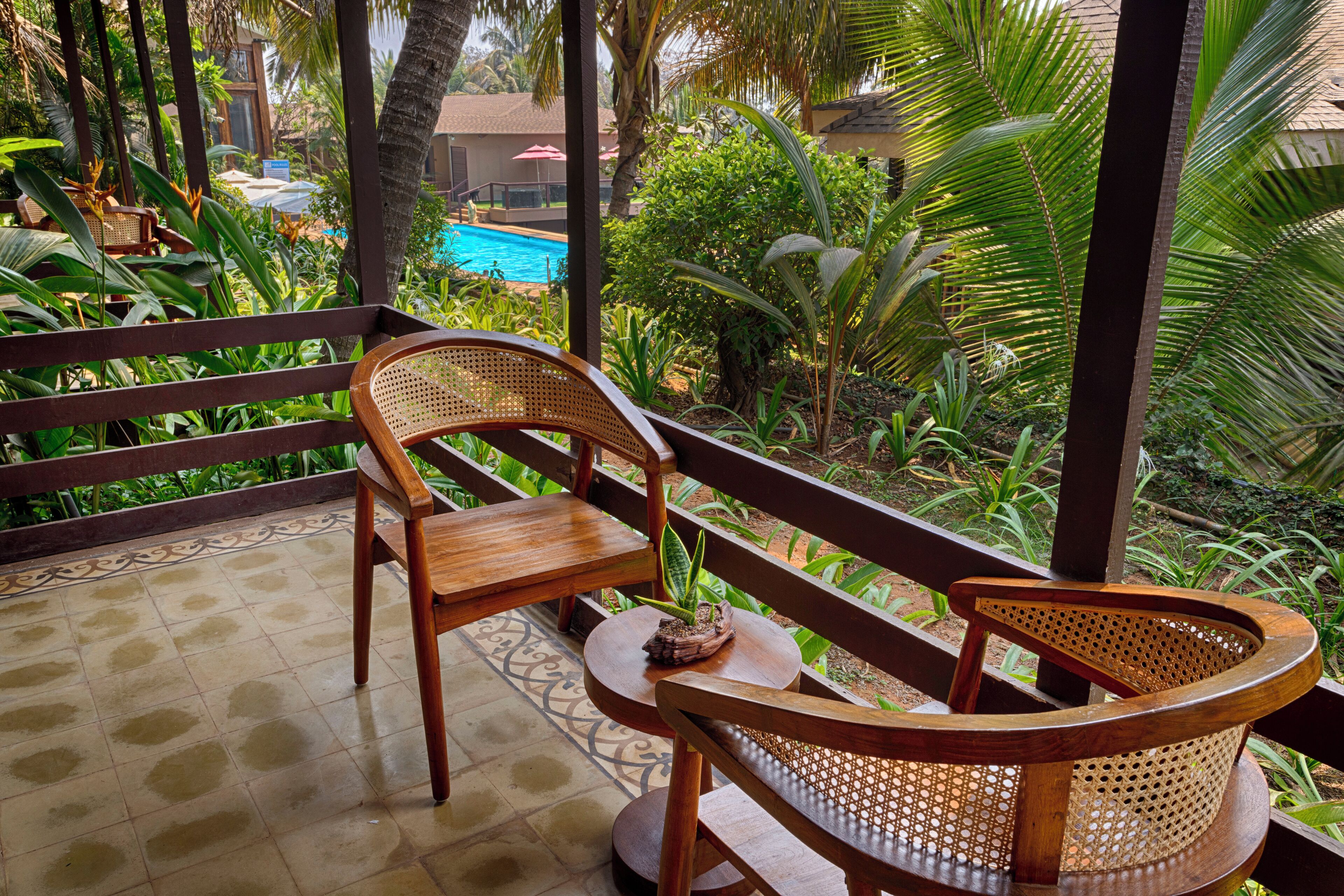 A wooden bench and chair set on a tiled patio with a view of a swimming pool and lush greenery.