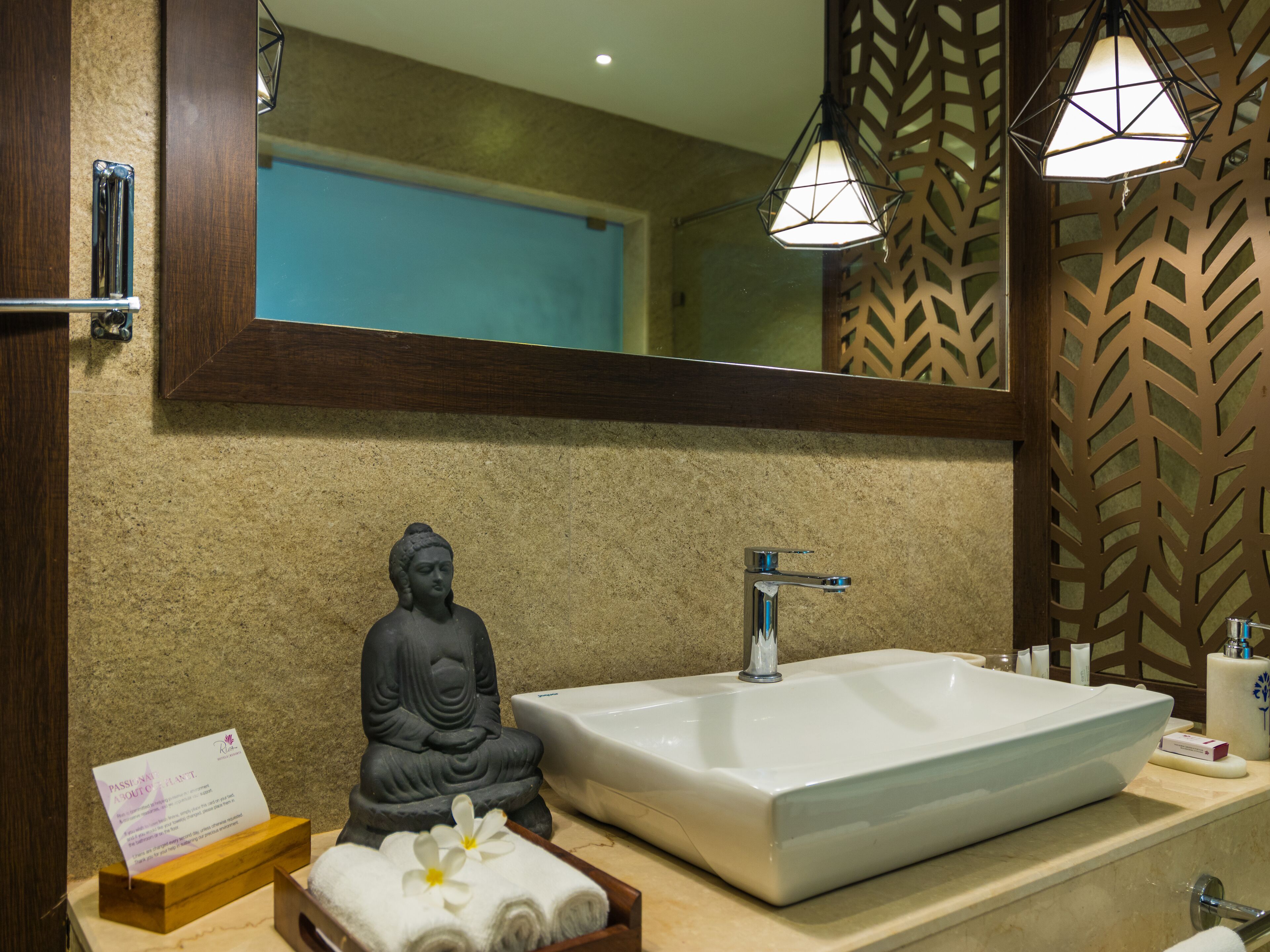 Un baño con un espejo grande, una estatua de Buda, un lavabo y un perchero para toallas.