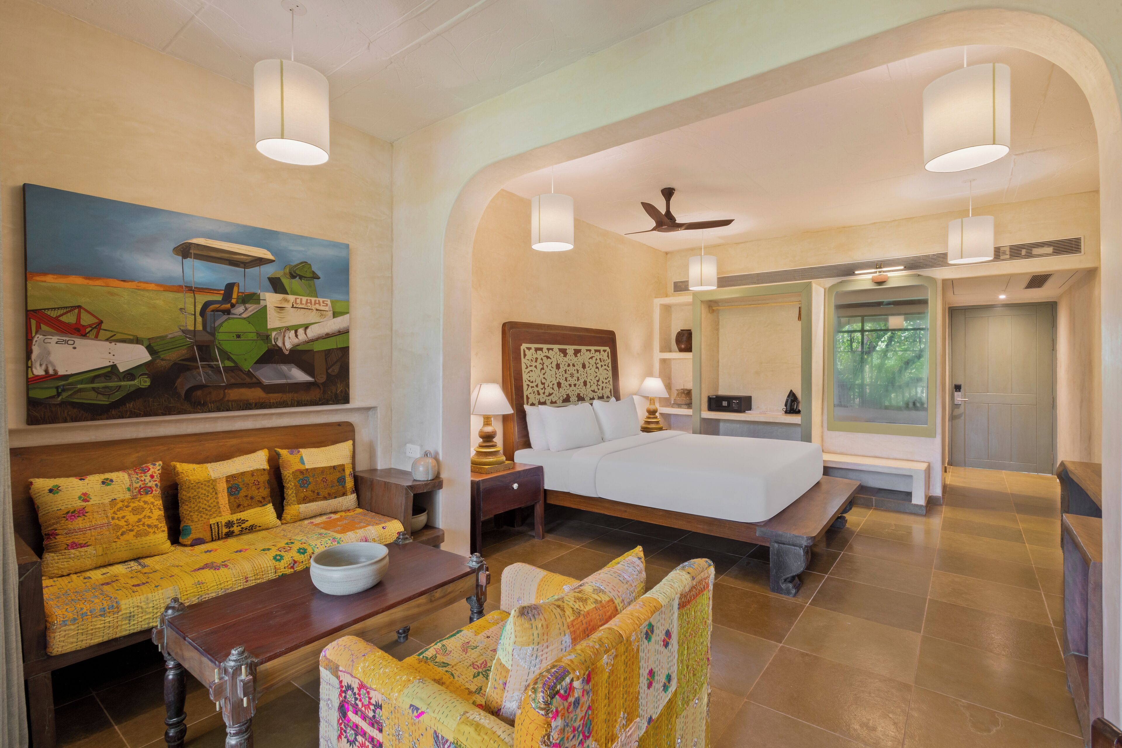 A hotel room with a large bed, a sofa, a dining table, and a painting on the wall.